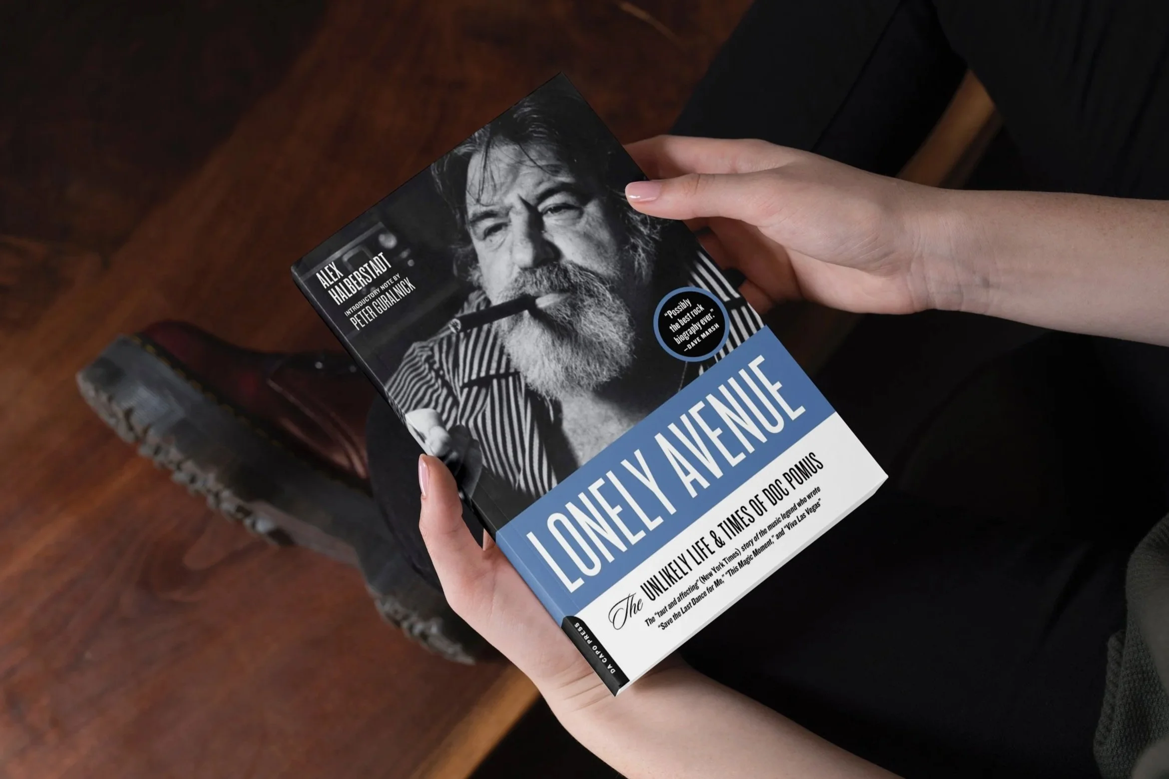 Person holding a book titled 'Lonely Avenue: The Unlikely Life and Times of Doc Pomus' with a black and white cover photo of Doc Pomus smoking a cigar.