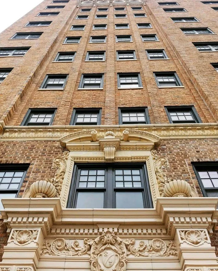 Low-angle view of Netherland, a tall brick building with multiple windows and ornate architectural details around a large central window.