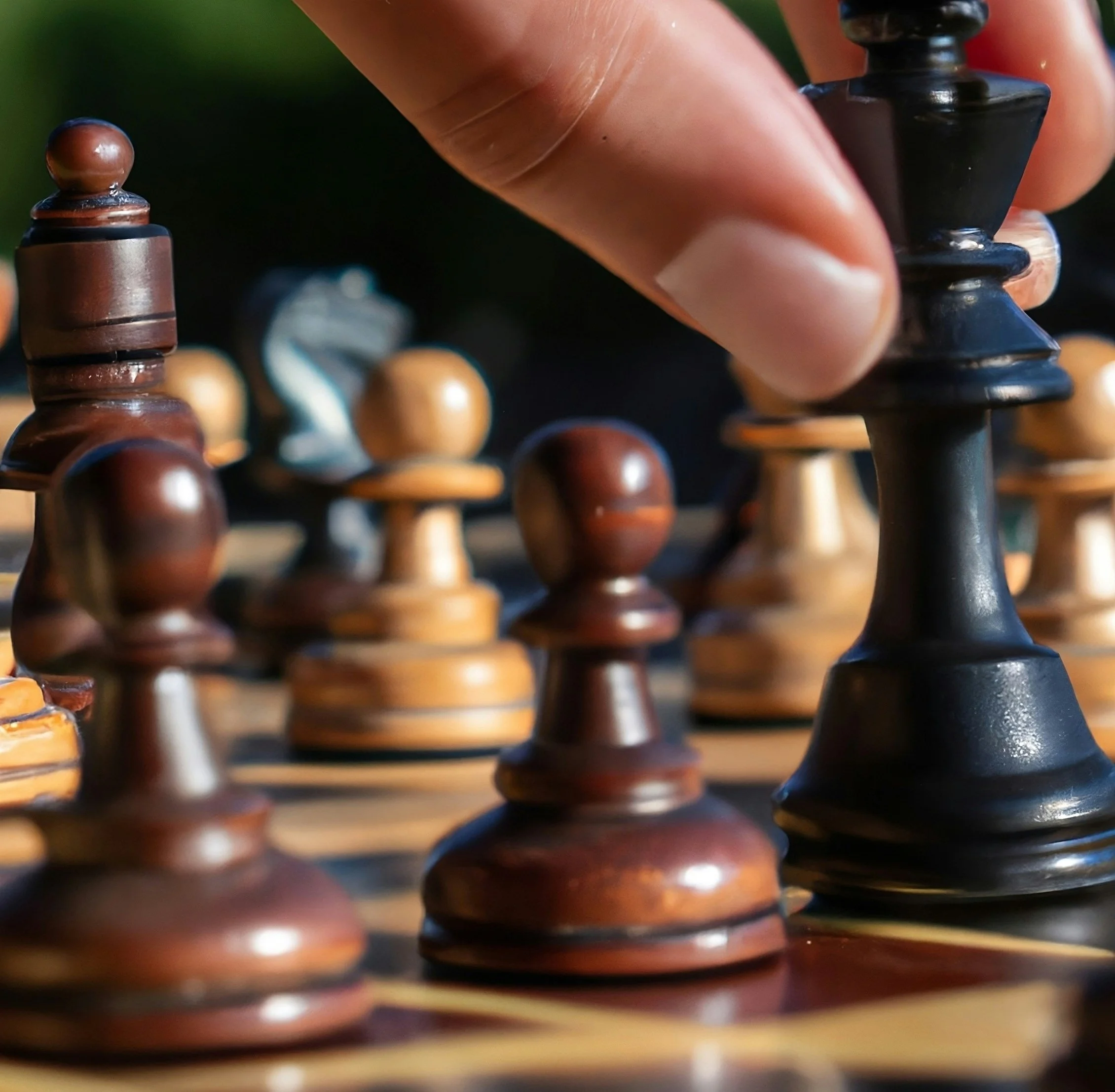 Close-up of a hand moving a black king chess piece on a wooden chessboard, with several brown and light-colored chess pieces in the background.