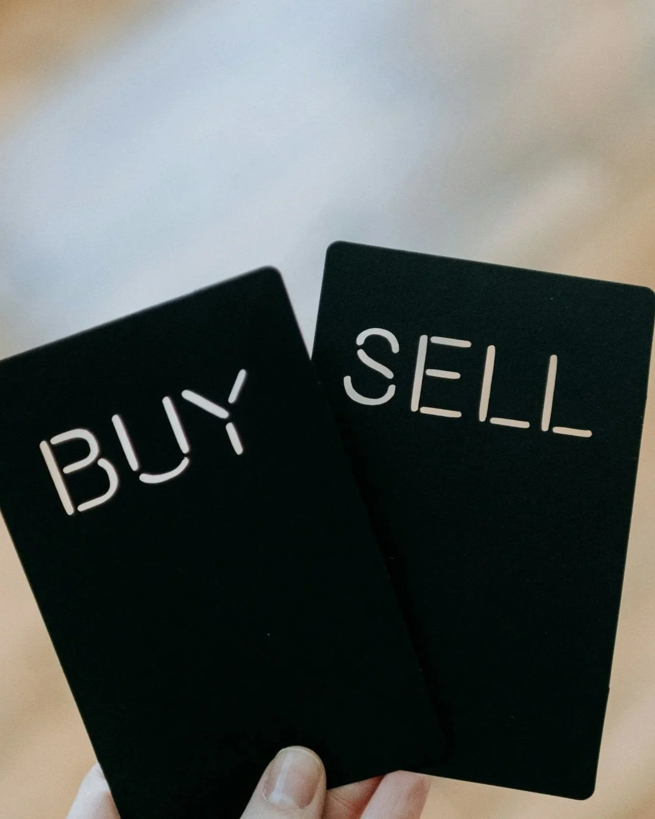 Black cards with white text that read 'BUY' and 'SELL' being held in a person's hand.