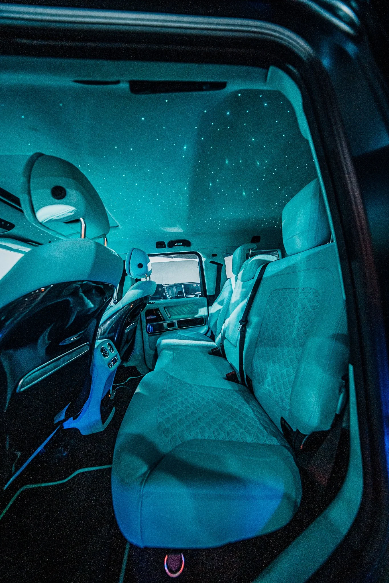 Inside a vehicle with white seats and a starry ceiling, viewed from the open door.