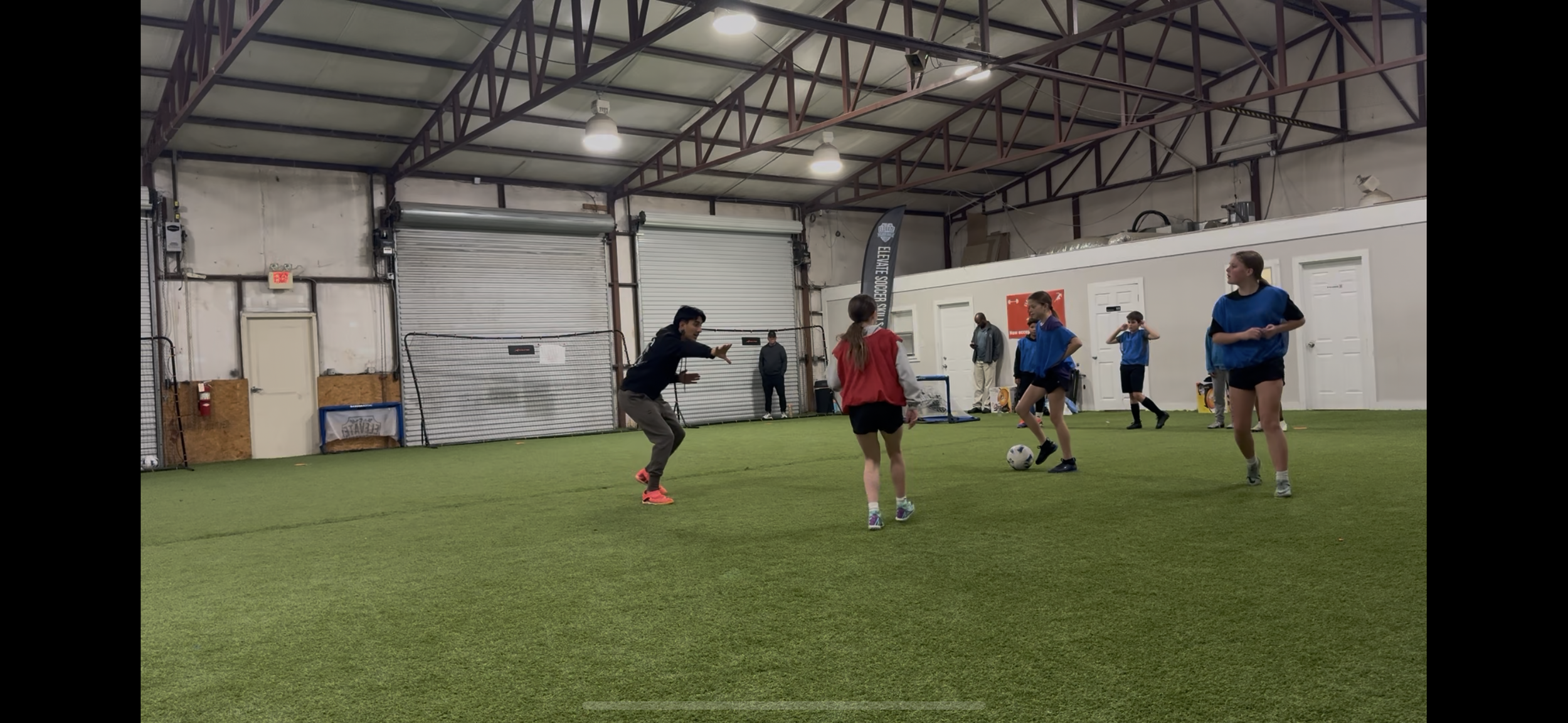 Indoor soccer training session with children and a coach on artificial turf field.