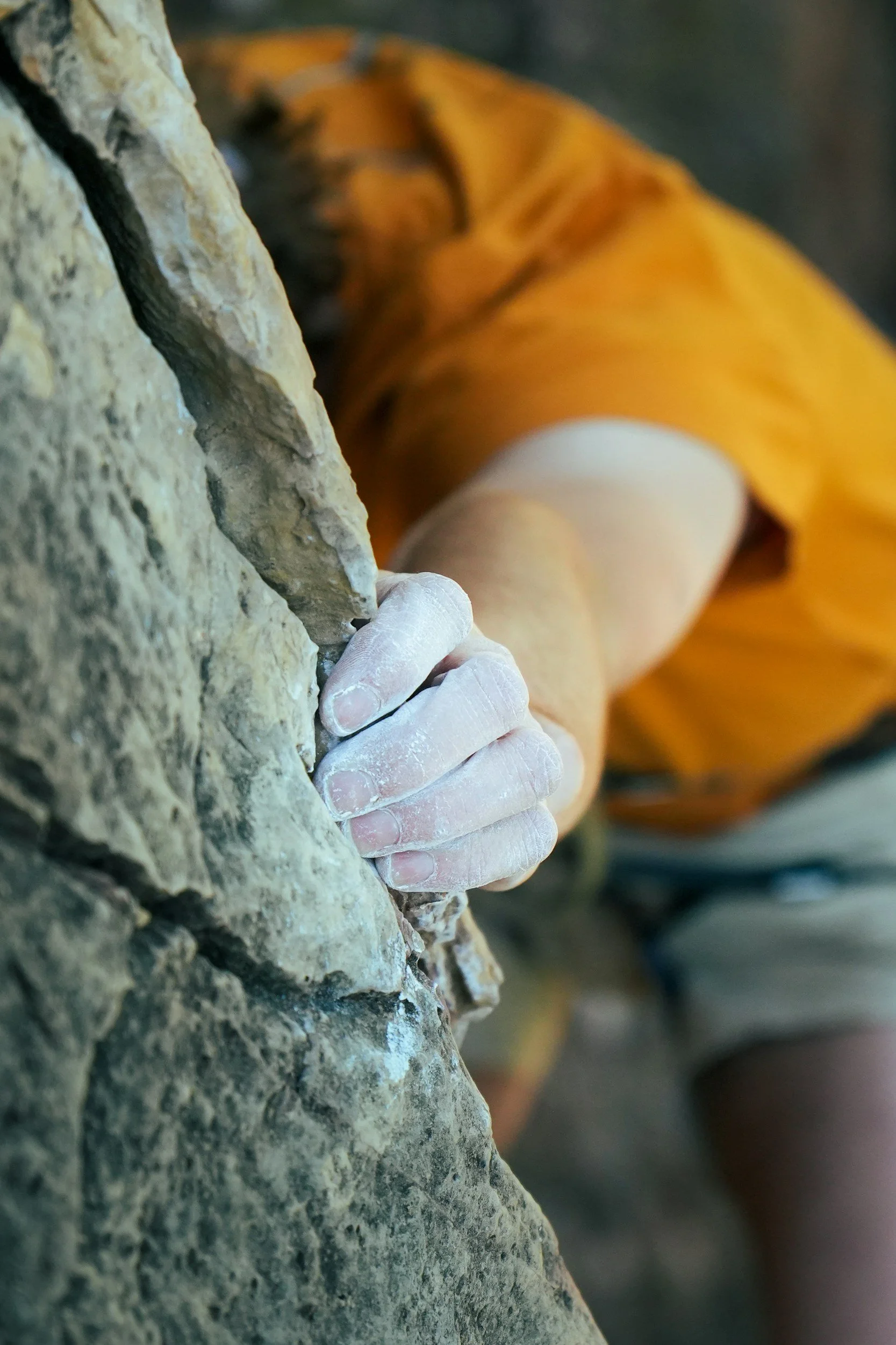 A person rock climbing outdoors, gripping a rock with their right hand.