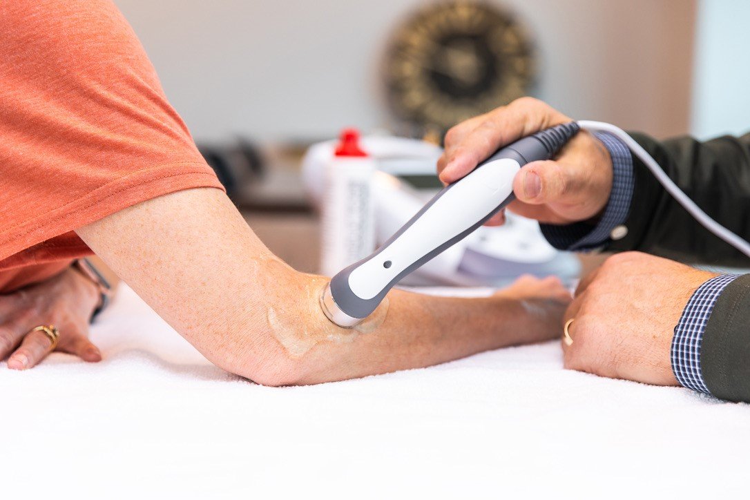 A healthcare worker uses a handheld device to perform a medical examination on an elderly person's arm.