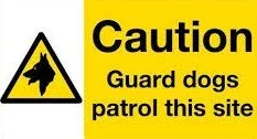 Yellow caution sign with a dog silhouette and text warning to guard dogs patrol this site.