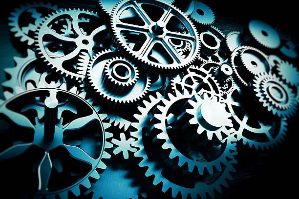 A collection of interconnected gears and cogs, with a dark background and some light highlights.
