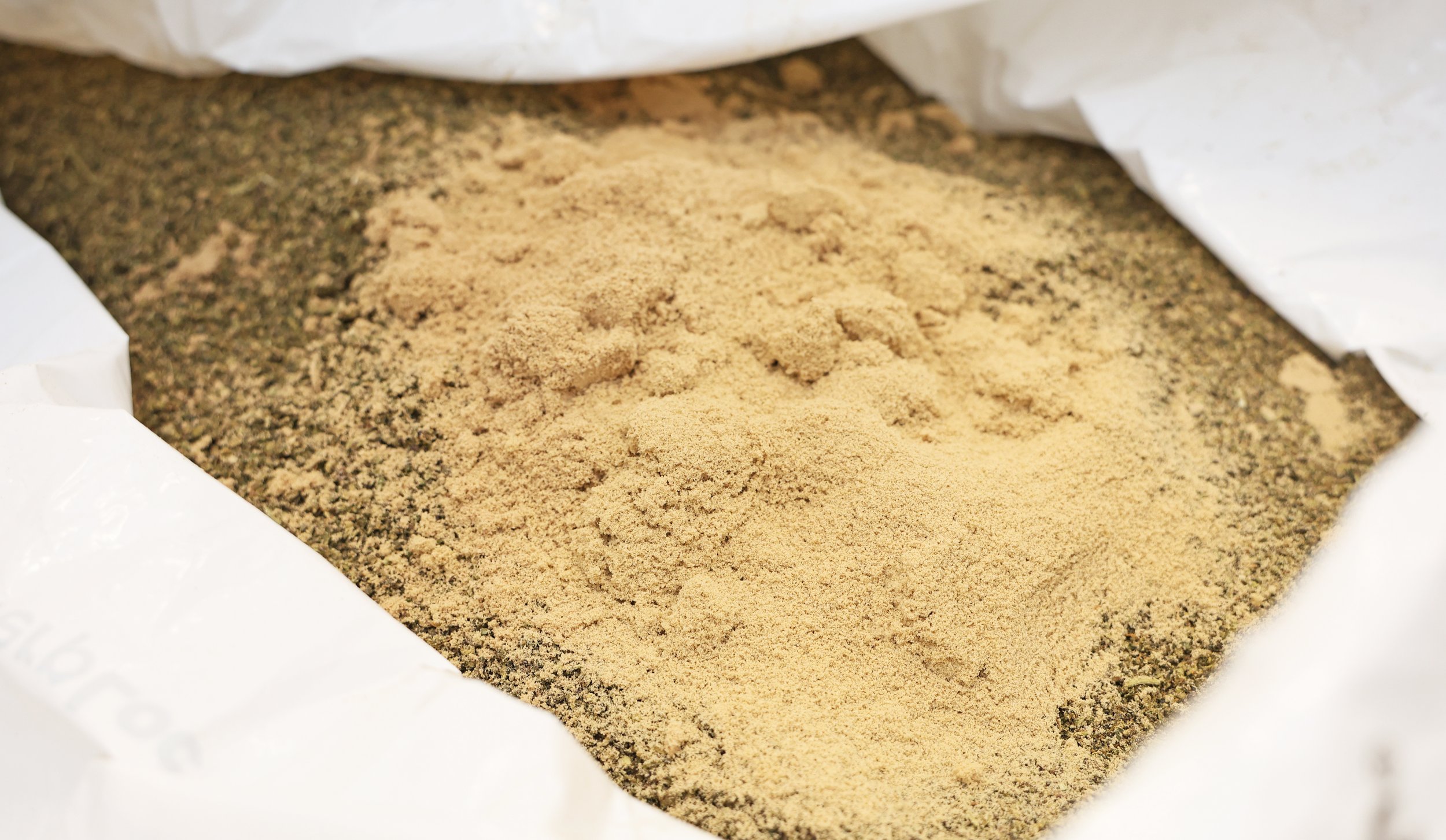 Close-up of a bag containing a mixture of brown and green herbs and spices, some of which are in powder form.