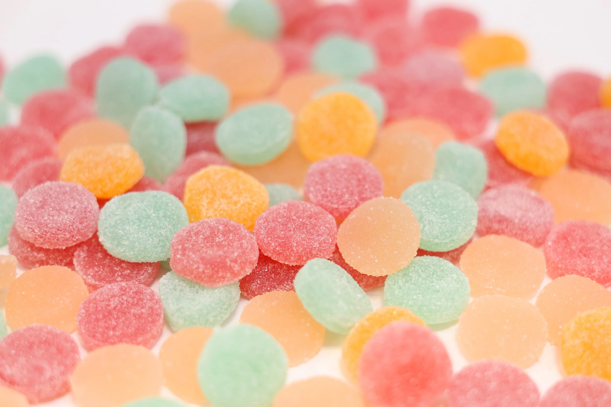 Colorful sugar-coated gummy candies in pastel shades of pink, orange, green, and yellow scattered on a white surface.