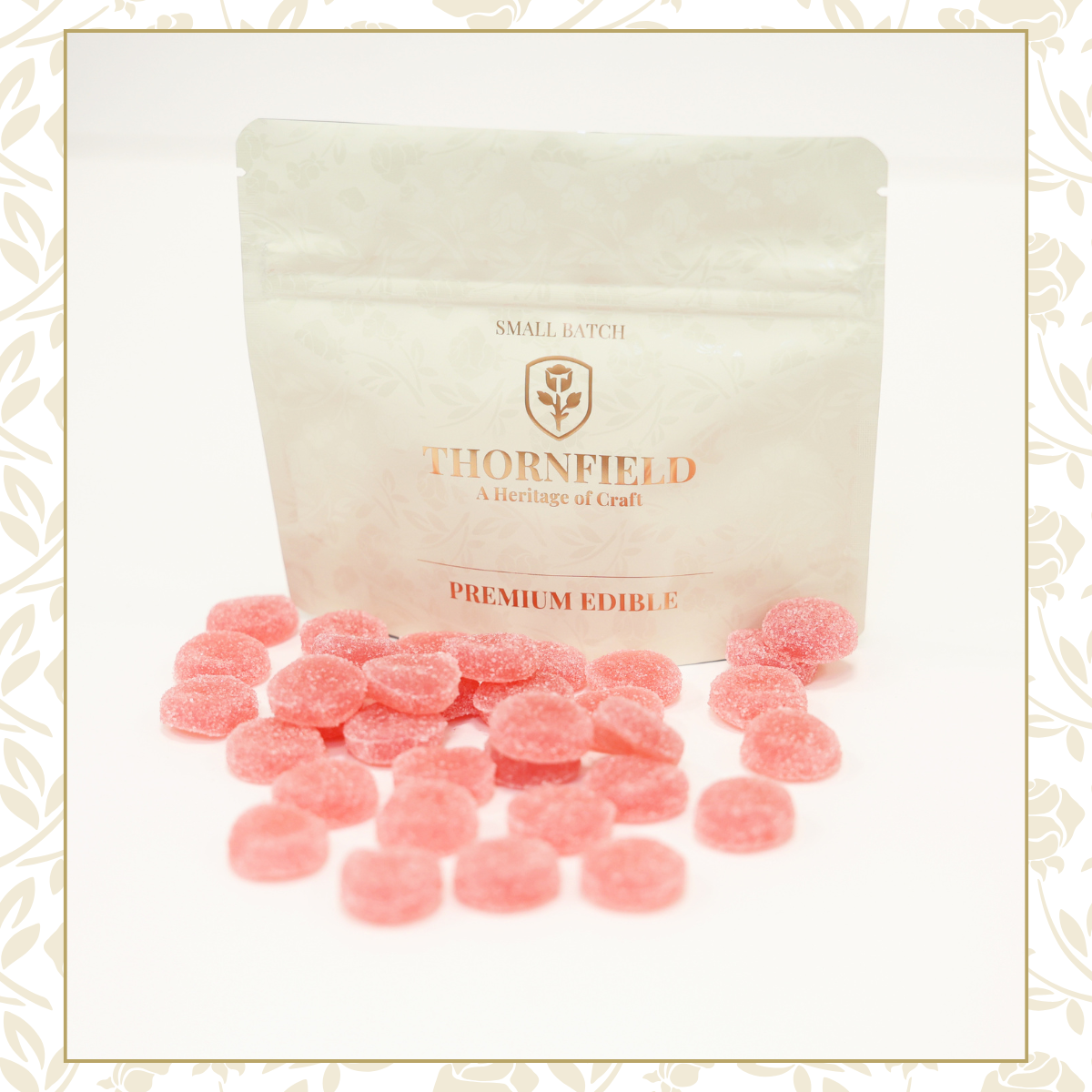 Pink, round, sugar-coated edible candies in front of a beige resealable bag labeled 'Thornfield Premium Edible' with a logo of a flower and the text 'Small Batch' and 'A Heritage of Craft.'