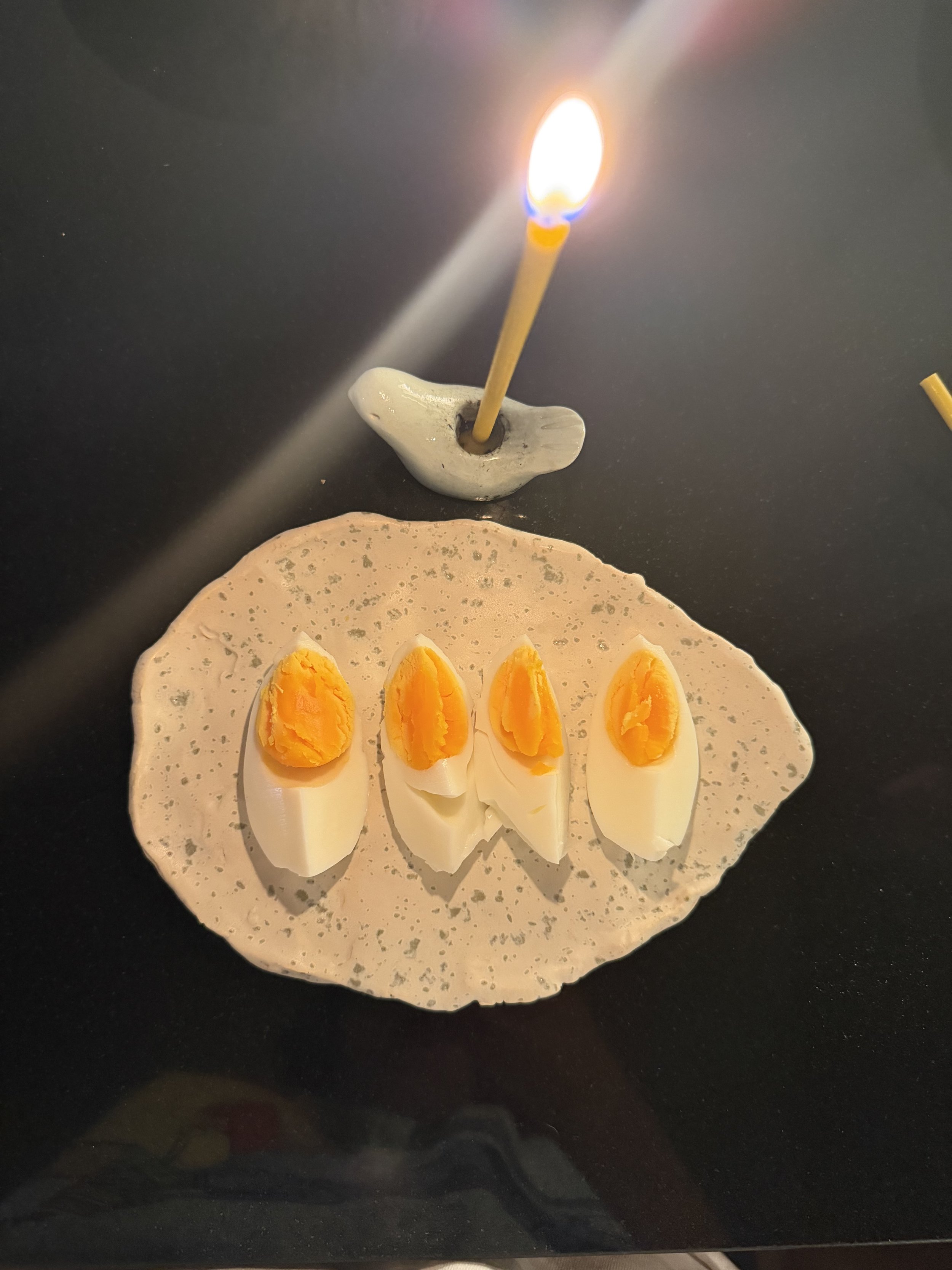 A piece of flatbread topped with sliced boiled eggs, with a lit birthday candle inserted into a small gray holder placed on the bread