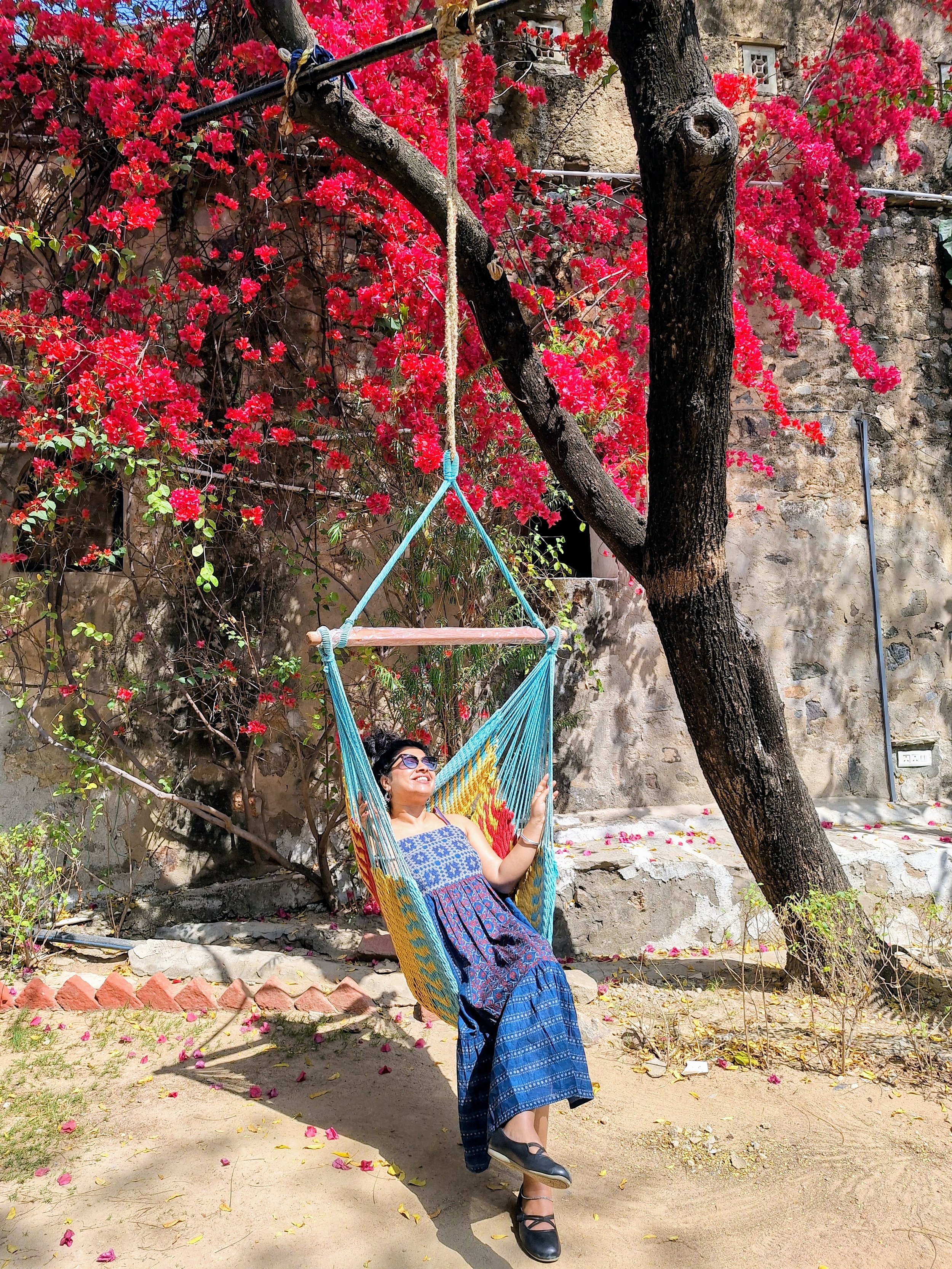 Dr. Pallabi Roy smiling in a tree swing amidst bright red flowers,