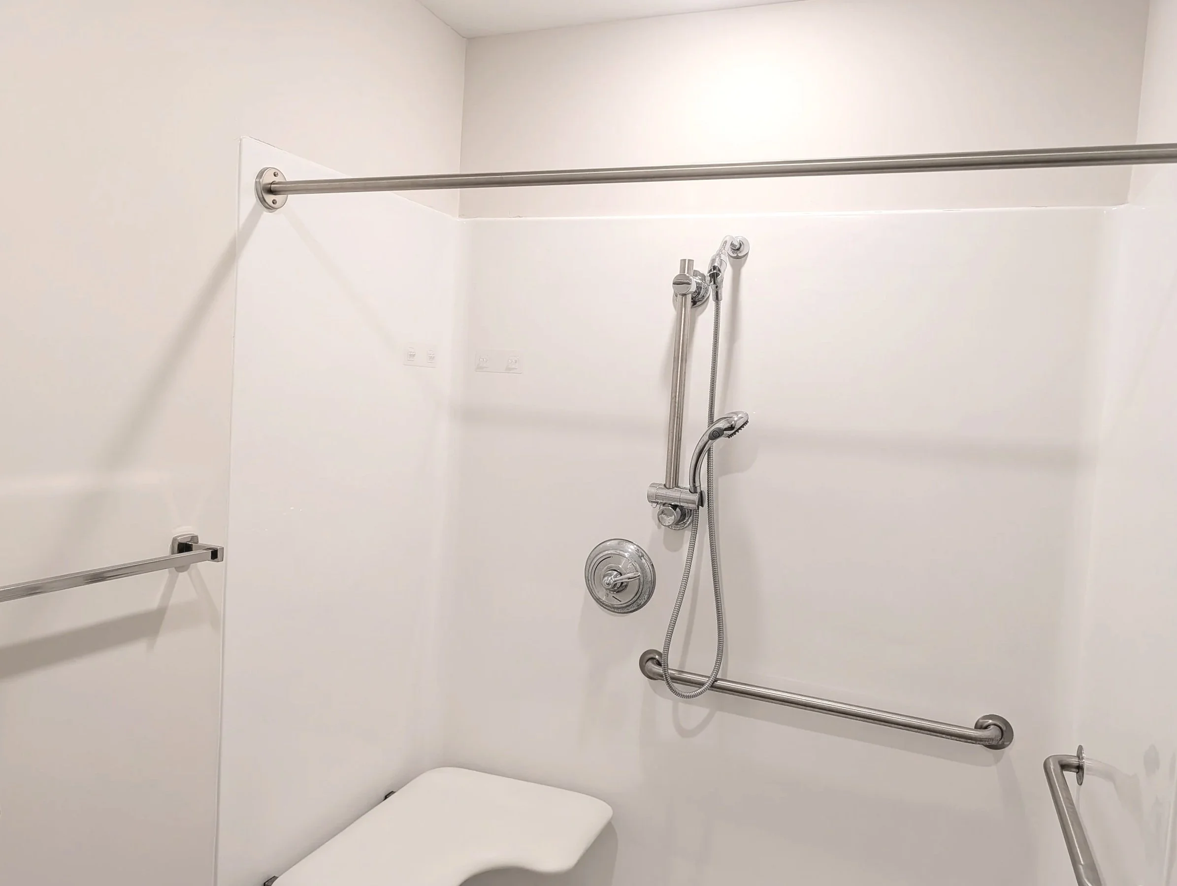 Shower room with white walls, a handheld showerhead, and grab bars.
