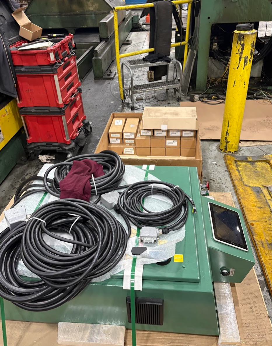 Industrial workspace with coiled cables, a tablet, red storage bins, and various boxes on a green work surface.