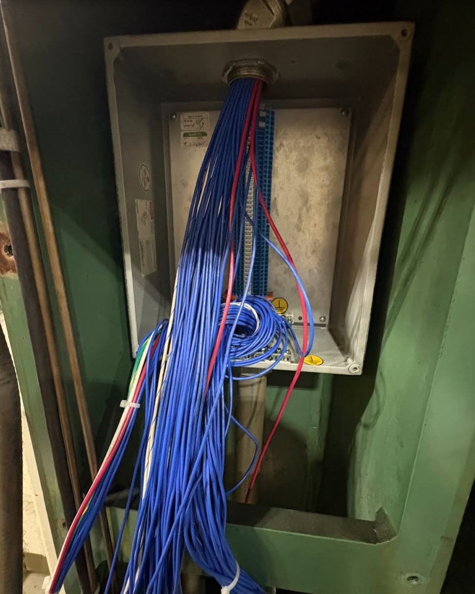 Electrical wiring with many blue, red and white cables inside an open green electrical box.