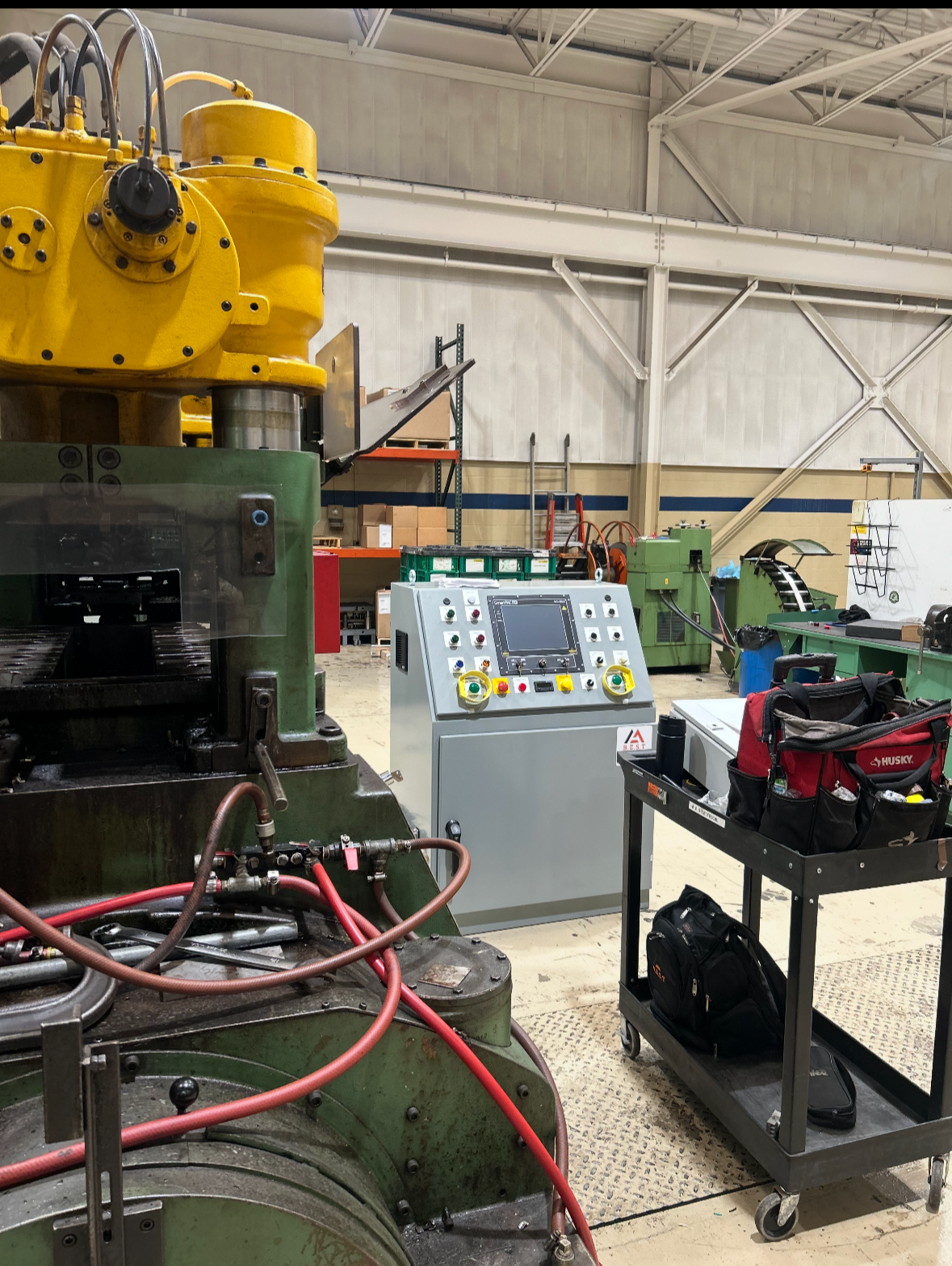 Industrial workshop with machinery, control panel, toolbox, and warehouse storage.