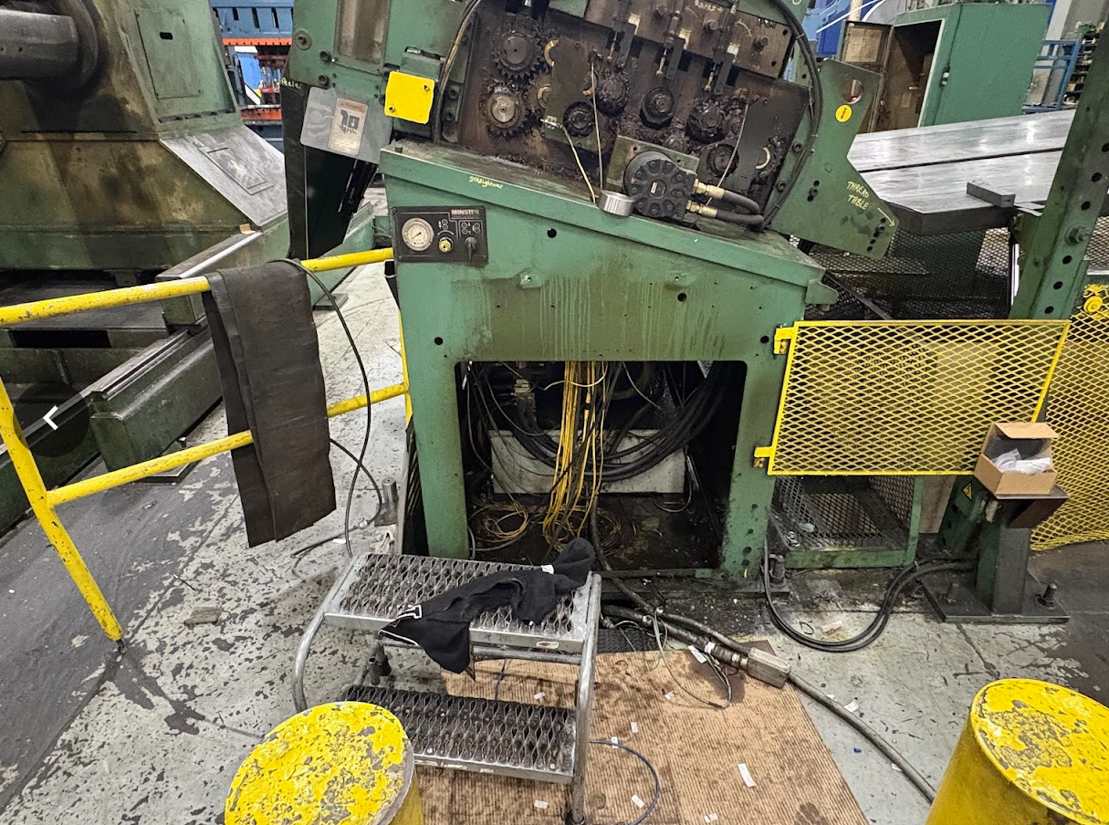 Industrial machine with wires, tools, and safety barriers in a workshop.