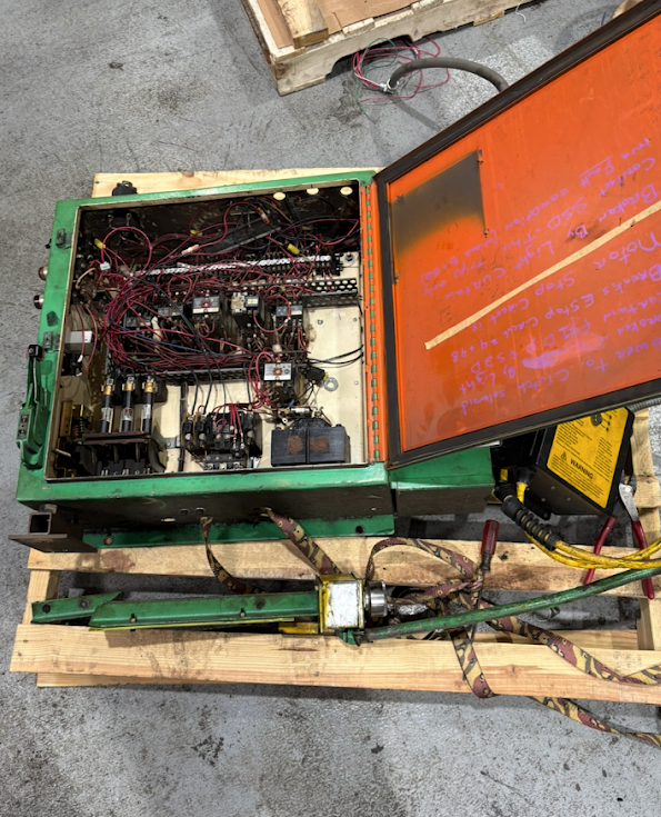 An open green industrial machine with numerous internal wires and components, mounted on a wooden pallet.