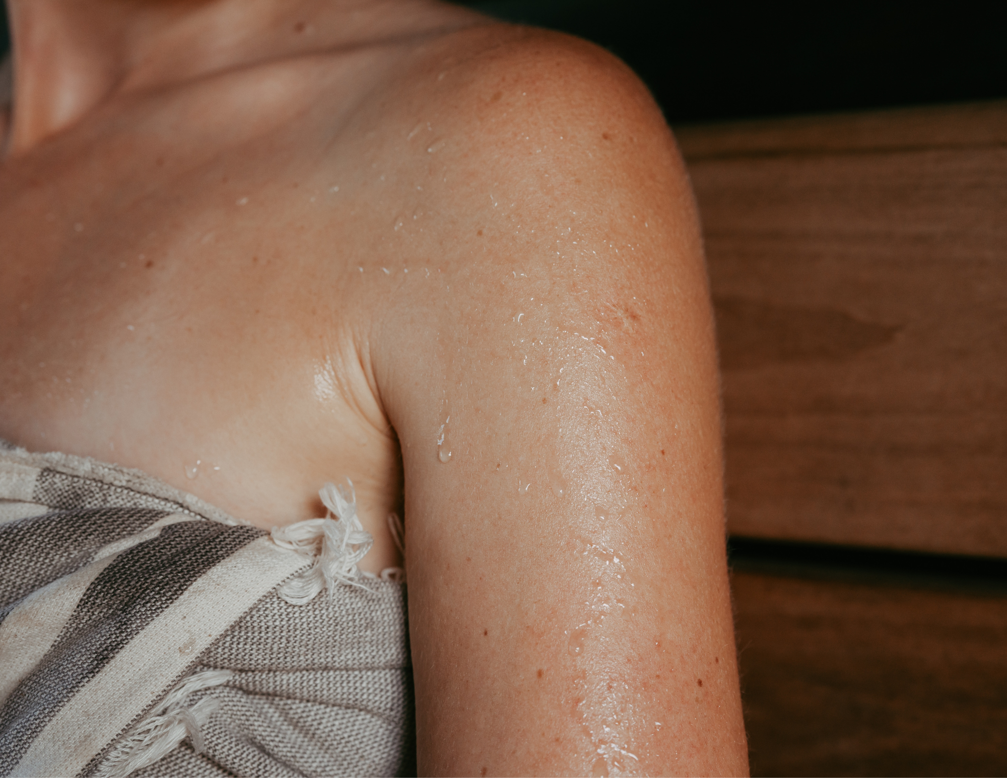 Close-up of a person's shoulder and upper arm with water droplets on skin, and part of a beige and brown striped garment.