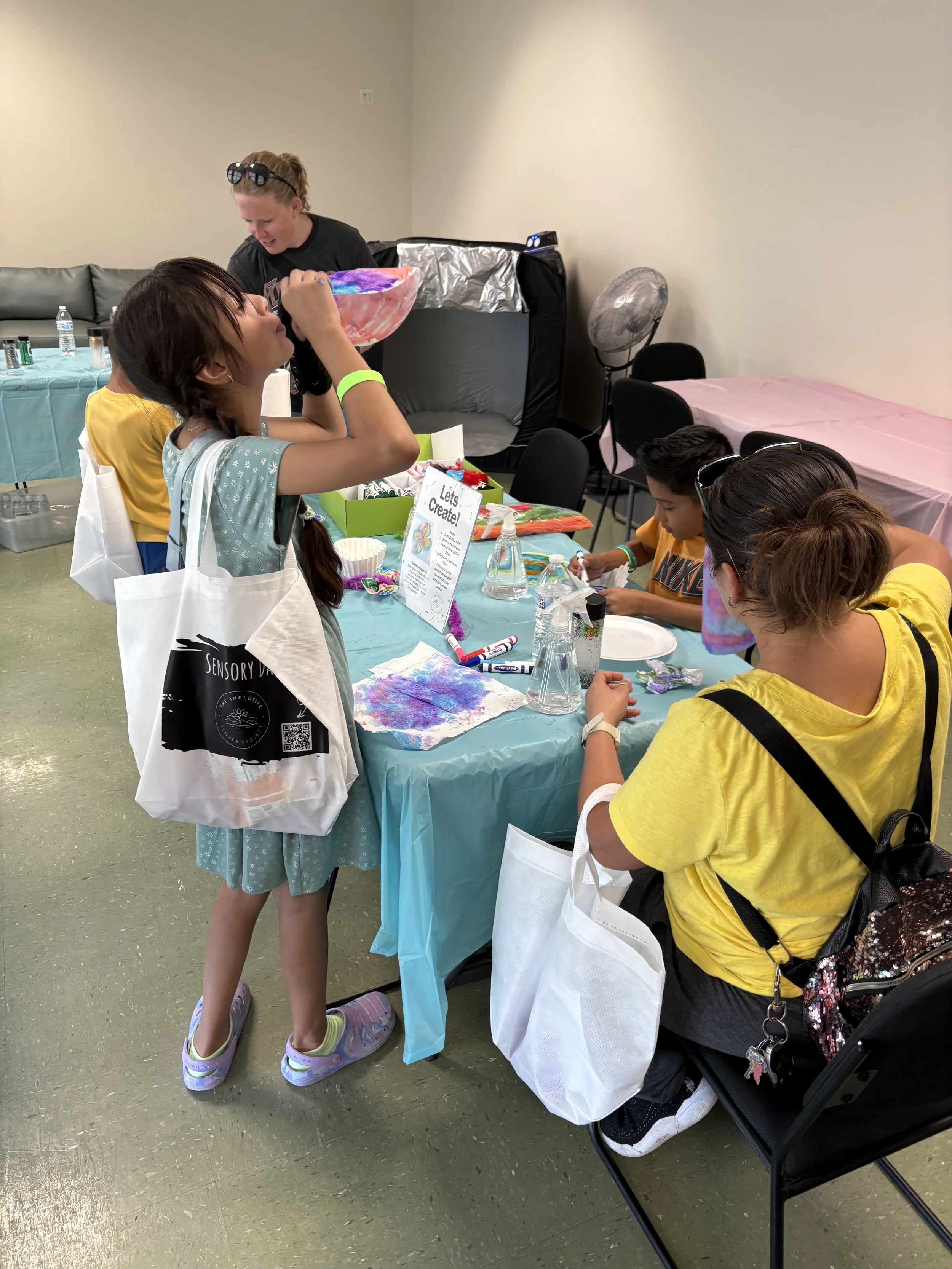 Children and adults participating in a crafting activity at a table during a birthday party, with supplies and decorations visible.