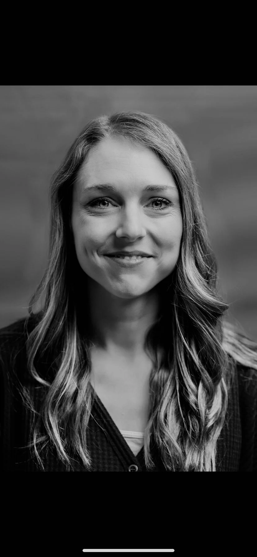 Black and white portrait of a woman with long wavy hair, smiling and looking at the camera.