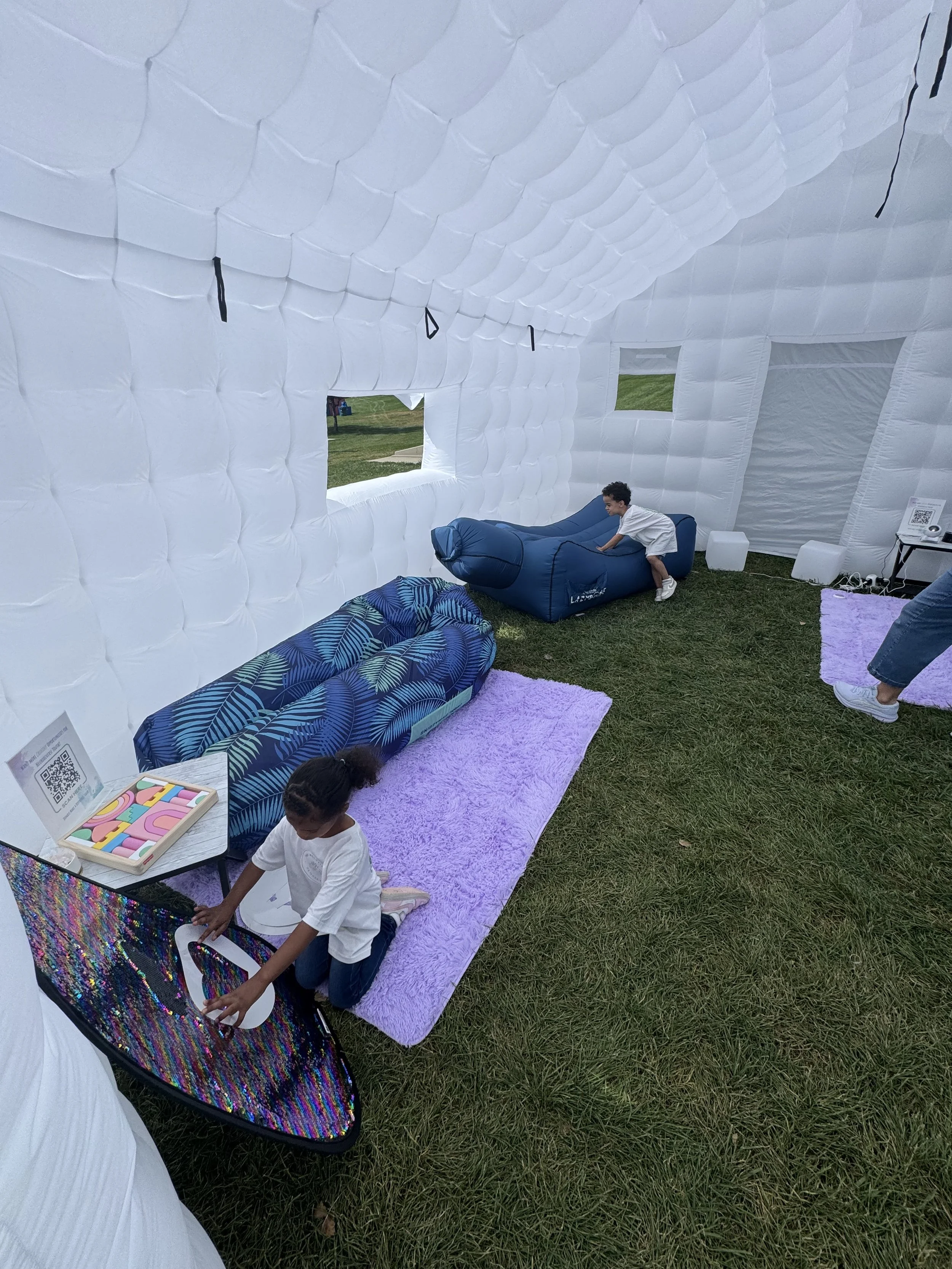 Children playing inside a white inflatable structure resembling a house, with sofas, a purple rug, and playful decor.