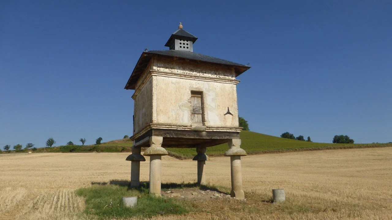 A pigeonnier, or dovecote, stands on four pillars in a field of wheat stubble.