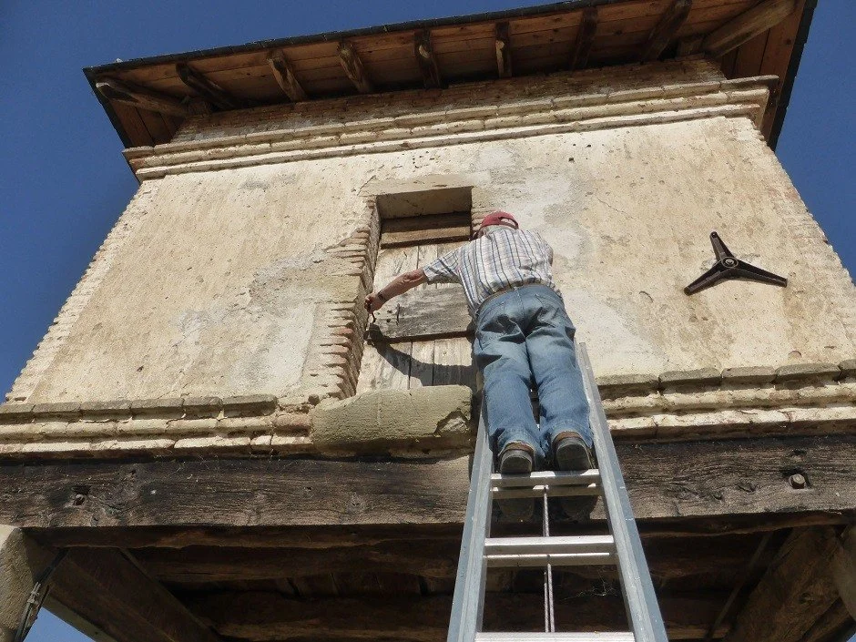 A man climbs a ladder to gain entry to a pigeonnier or dovecote.