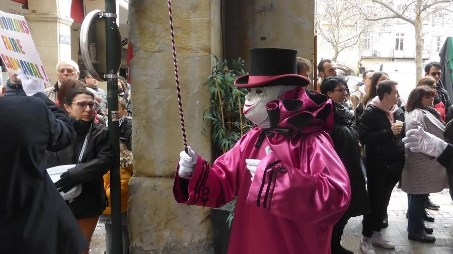 Wearing a cerise costume and holding a striped wand, this dancer is taking part in the Carnival of Limoux.