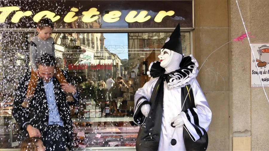 A dancer in a black and white costume throws confetti over a man and boy at the Carnival of Limoux.