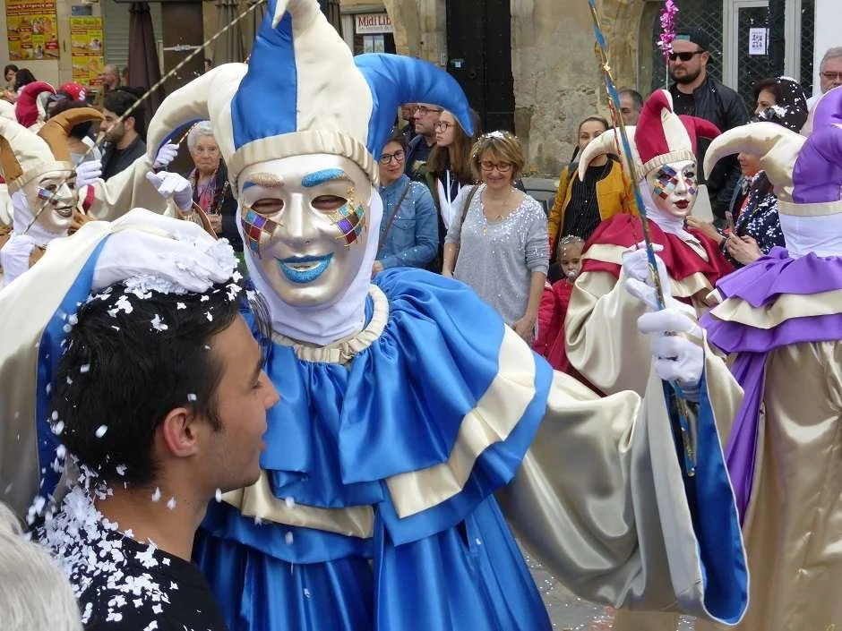 A carnival-costumed figure covers a boy's head with white confetti at the Carnival de Limoux.