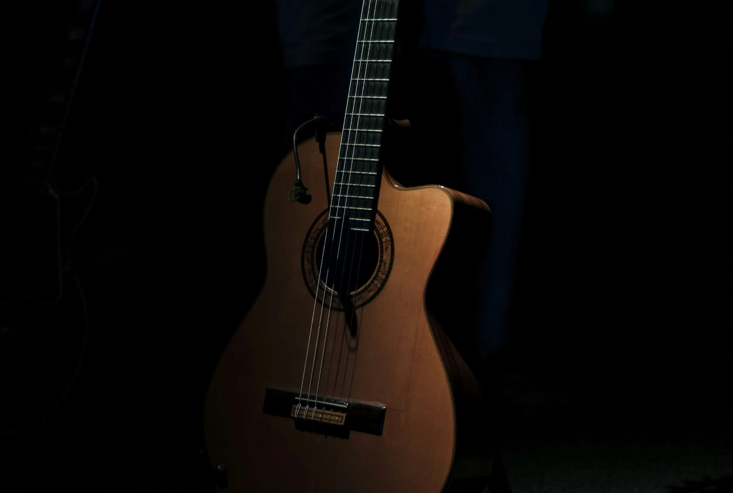 An acoustic guitar with a microphone nearby, partially illuminated against a dark background.