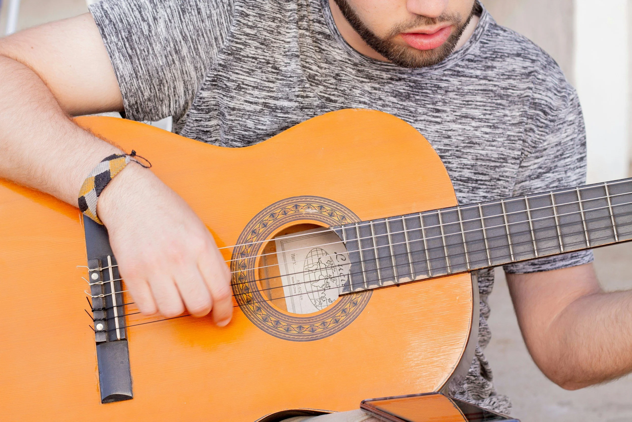 A man wearing a gray striped t-shirt playing an orange acoustic guitar.