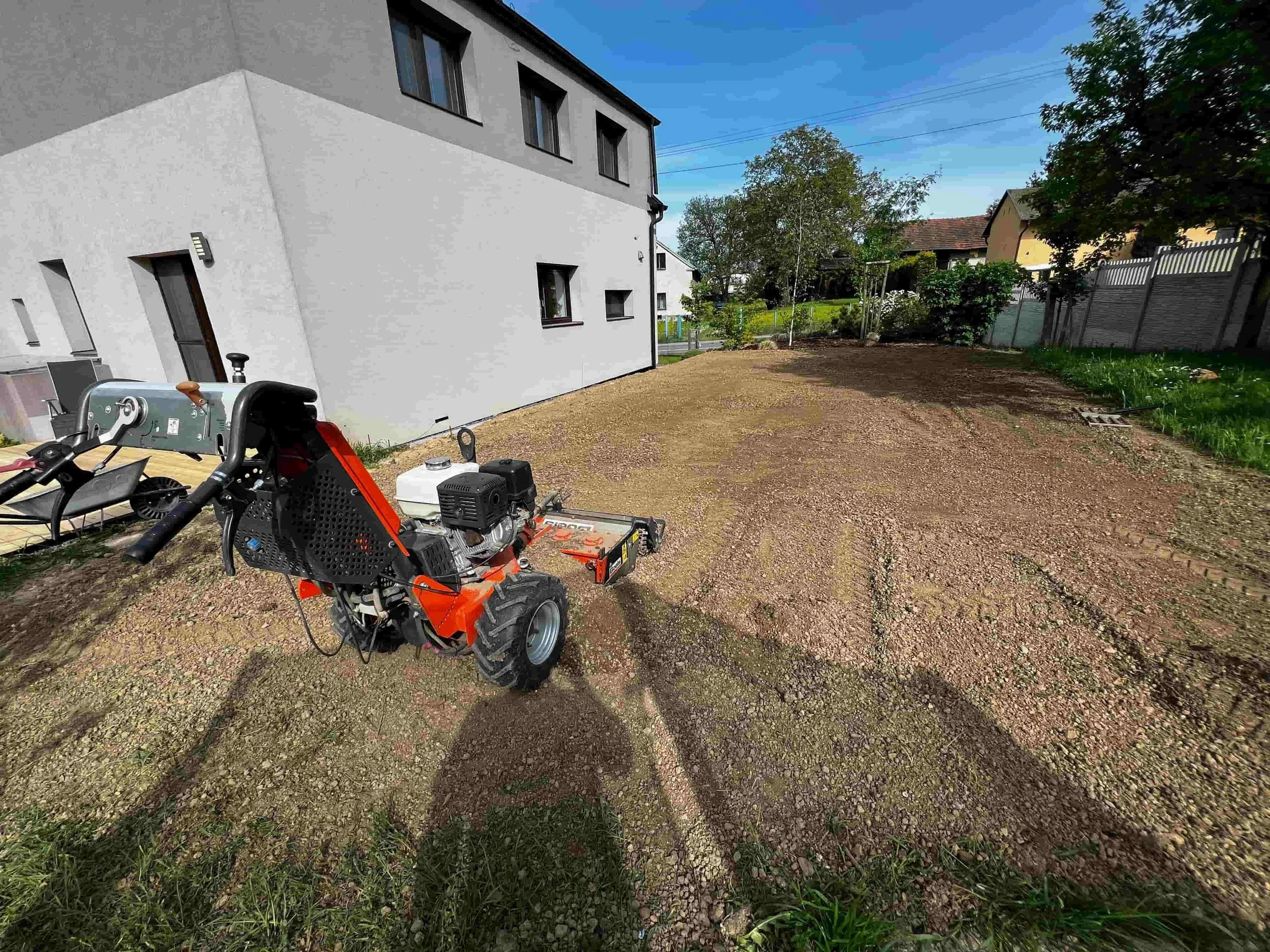 Rozpracovaná zahrada u moderního bílého domu – terénní úpravy, stavební technika a část trávníku před dokončením.