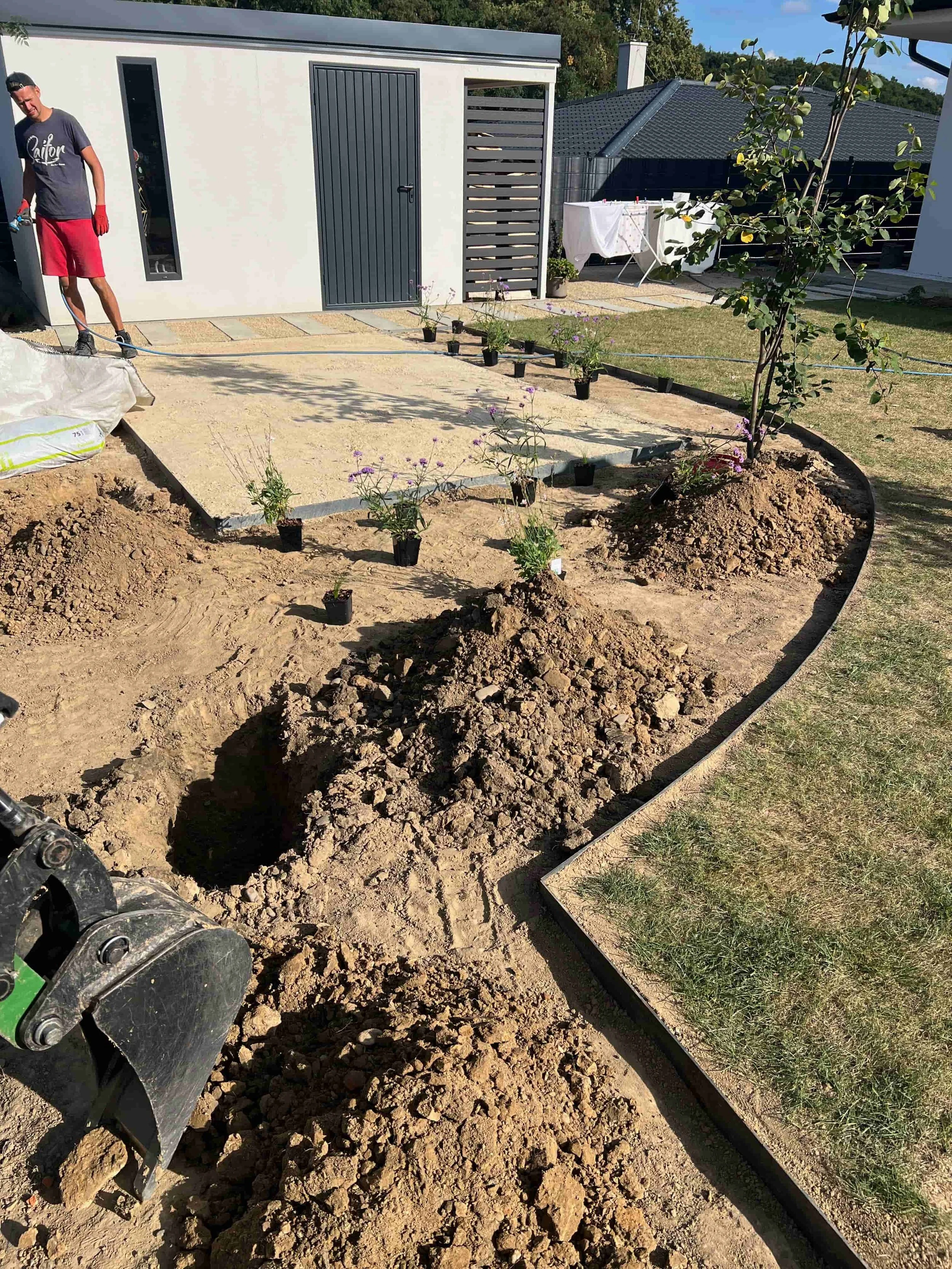 Práce na zahradě při realizaci – zahradník při úpravách kolem zahradního domku za slunného dne.