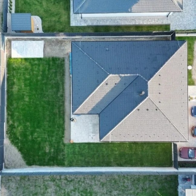 Letecký pohled na rodinný dům se zahradou, trávníkem a příjezdovou cestou, v okolí další domy a ulice.