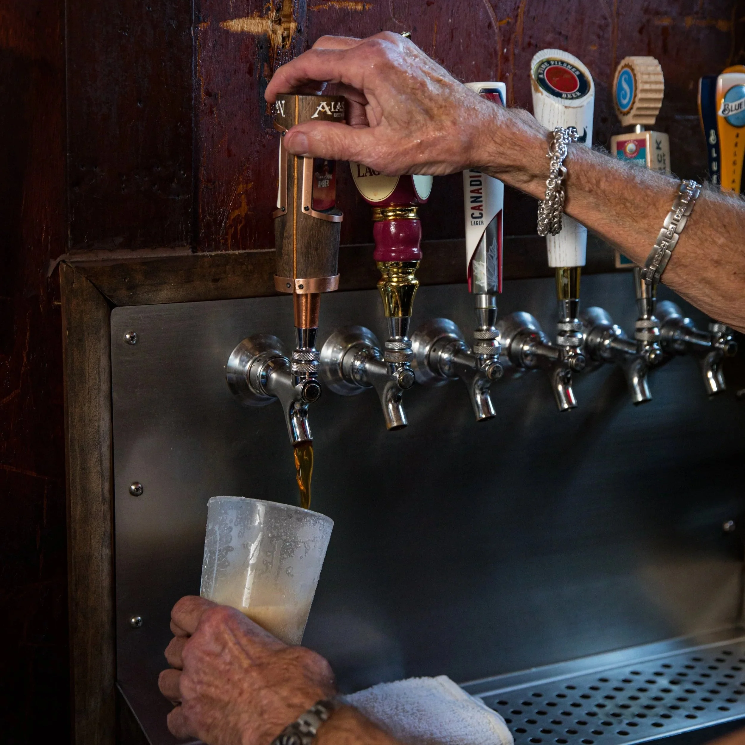 An elderly person's hand is filling a glass with dark beer from a beer tap at a bar or pub.