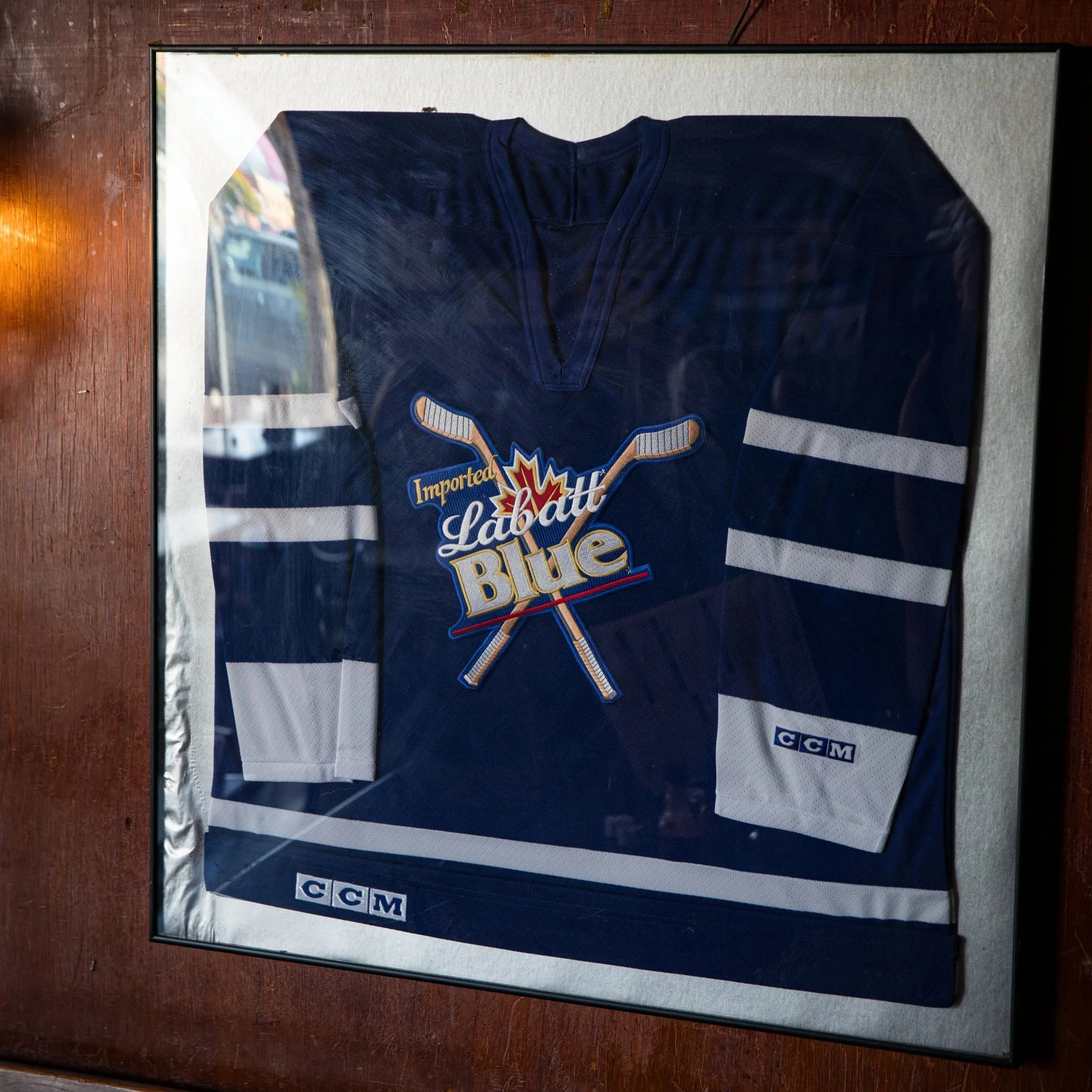 Framed hockey jersey with blue color, white stripes on sleeves, and a logo featuring crossed hockey sticks and a maple leaf, with the text 'Imported Labatt Blue' on the front.
