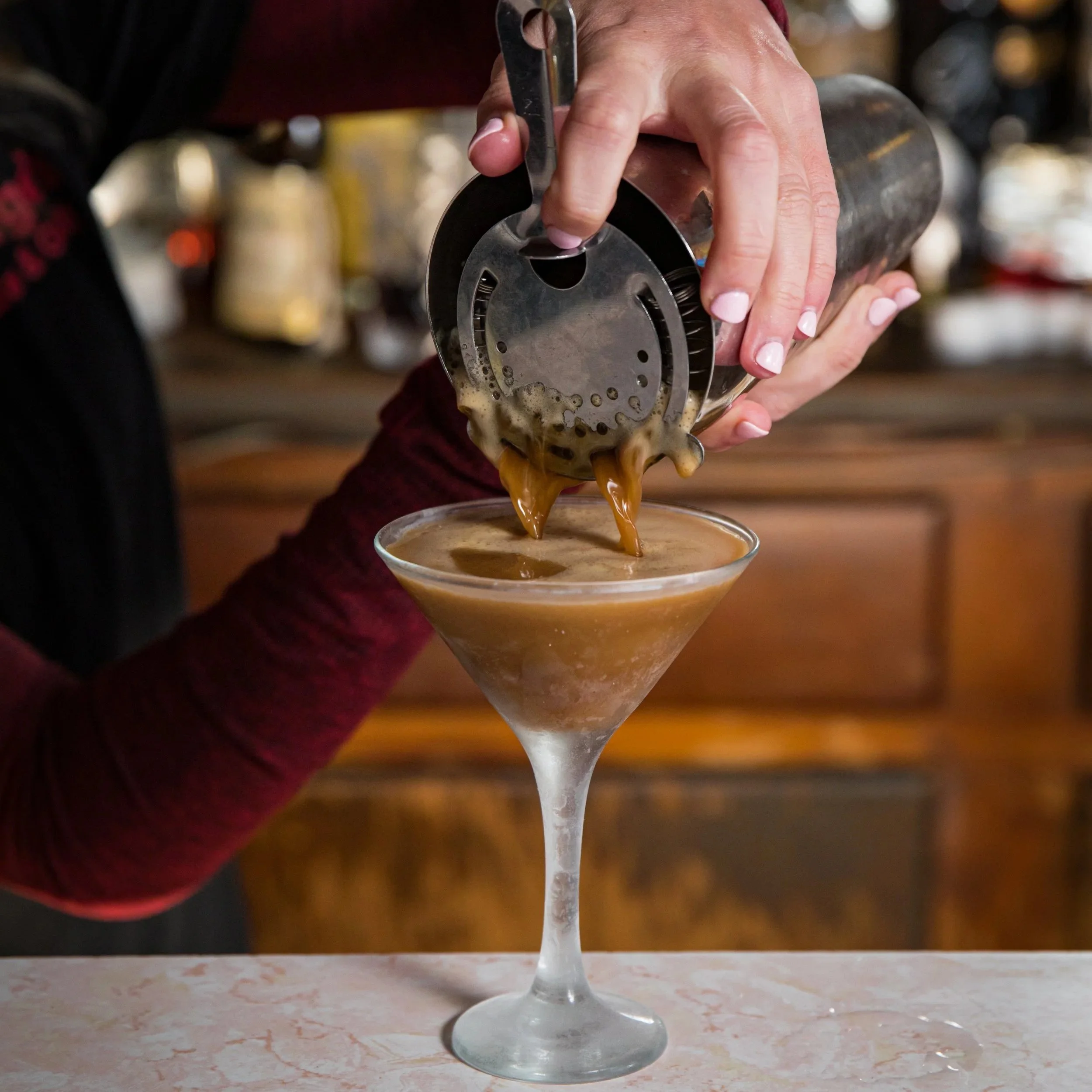 A bartender pours a mixed coffee drink into a martini glass.