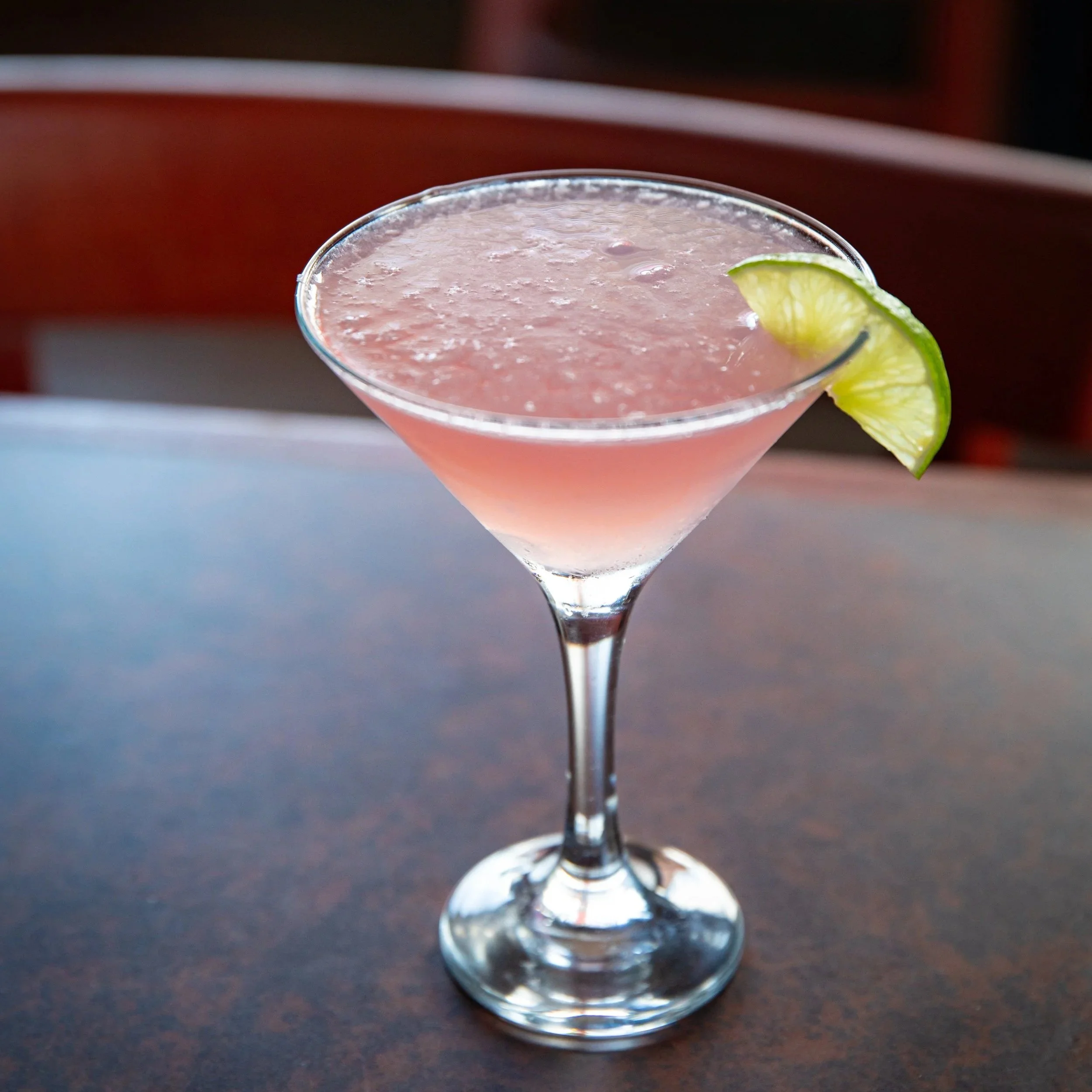 Pink cocktail in a martini glass garnished with a lime wedge.