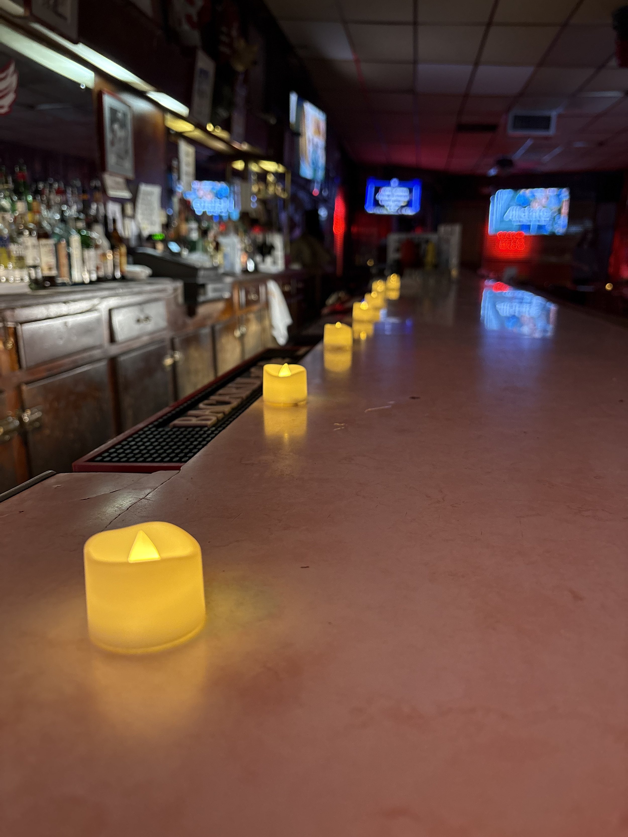 Empty bar counter with yellow candle lights and neon signs in background.