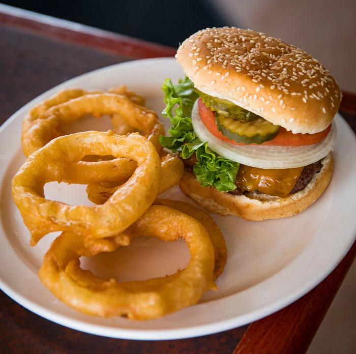 A plate of onion rings and a cheeseburger with lettuce, tomato, pickles, onion, and a sesame seed bun.