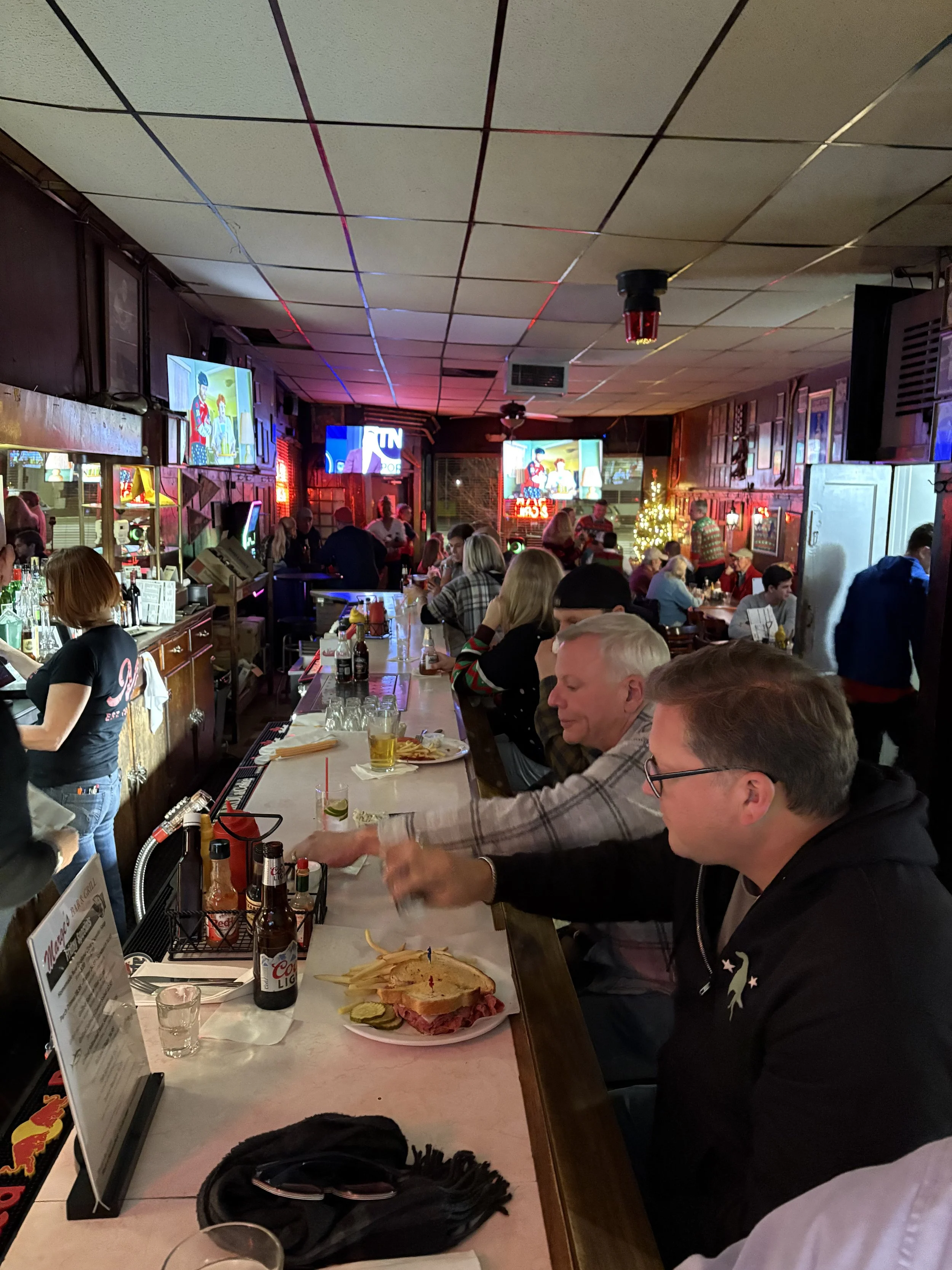 People sitting at a bar with food and drinks, watching TV screens in a lively, decorated pub.