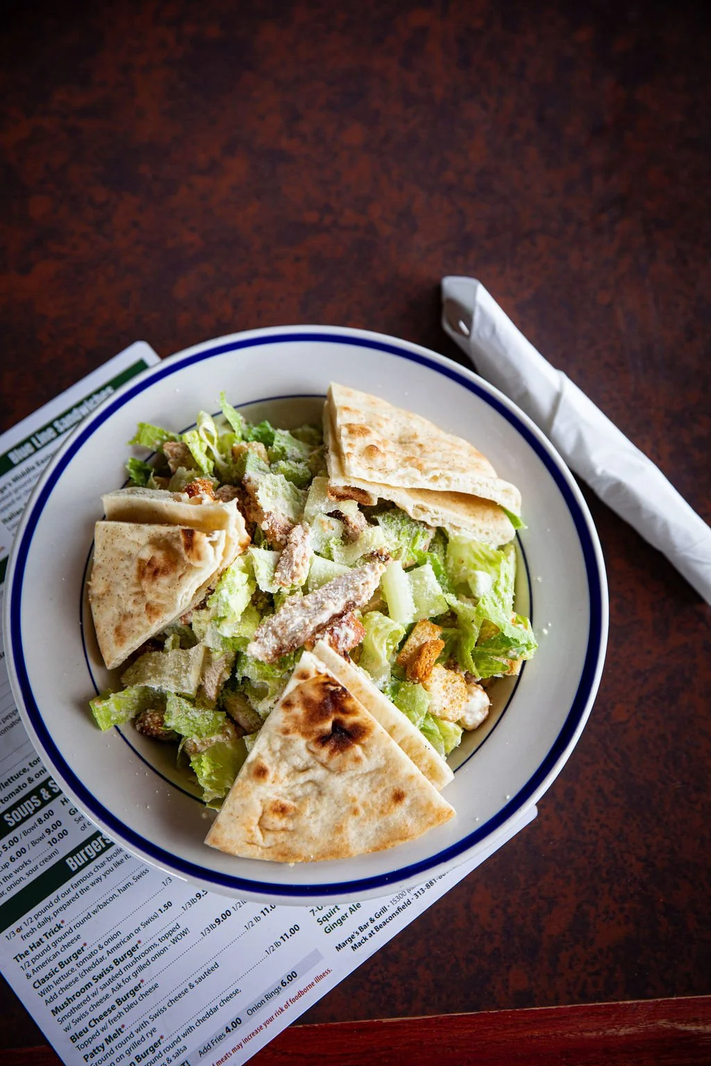 A bowl of salad with lettuce, shredded cheese, and pieces of flatbread on top.