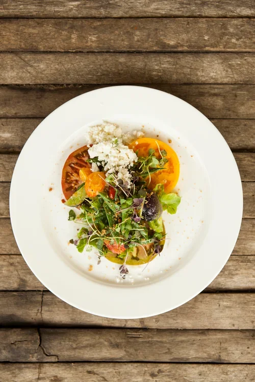 Plate of fresh salad with tomatoes, greens, crumbled cheese, and a soft-boiled egg on a wooden table.