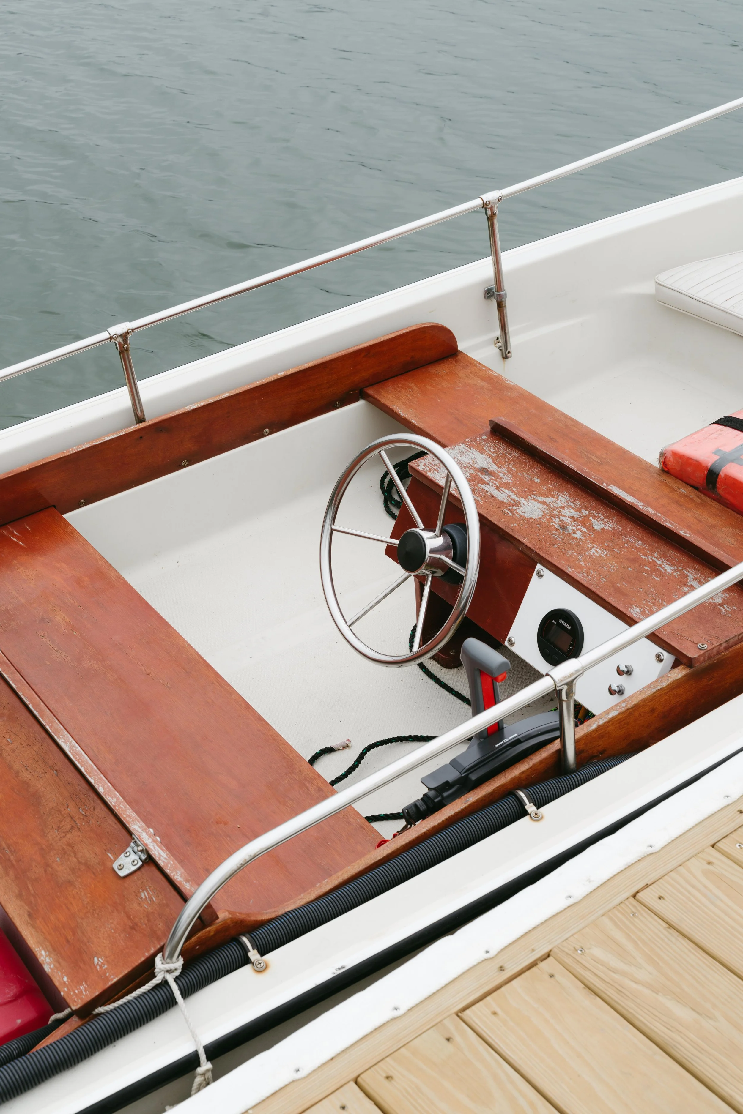 The interior of a small boat on the water, showing a wooden steering wheel, a dashboard, and seating area with wooden panels.