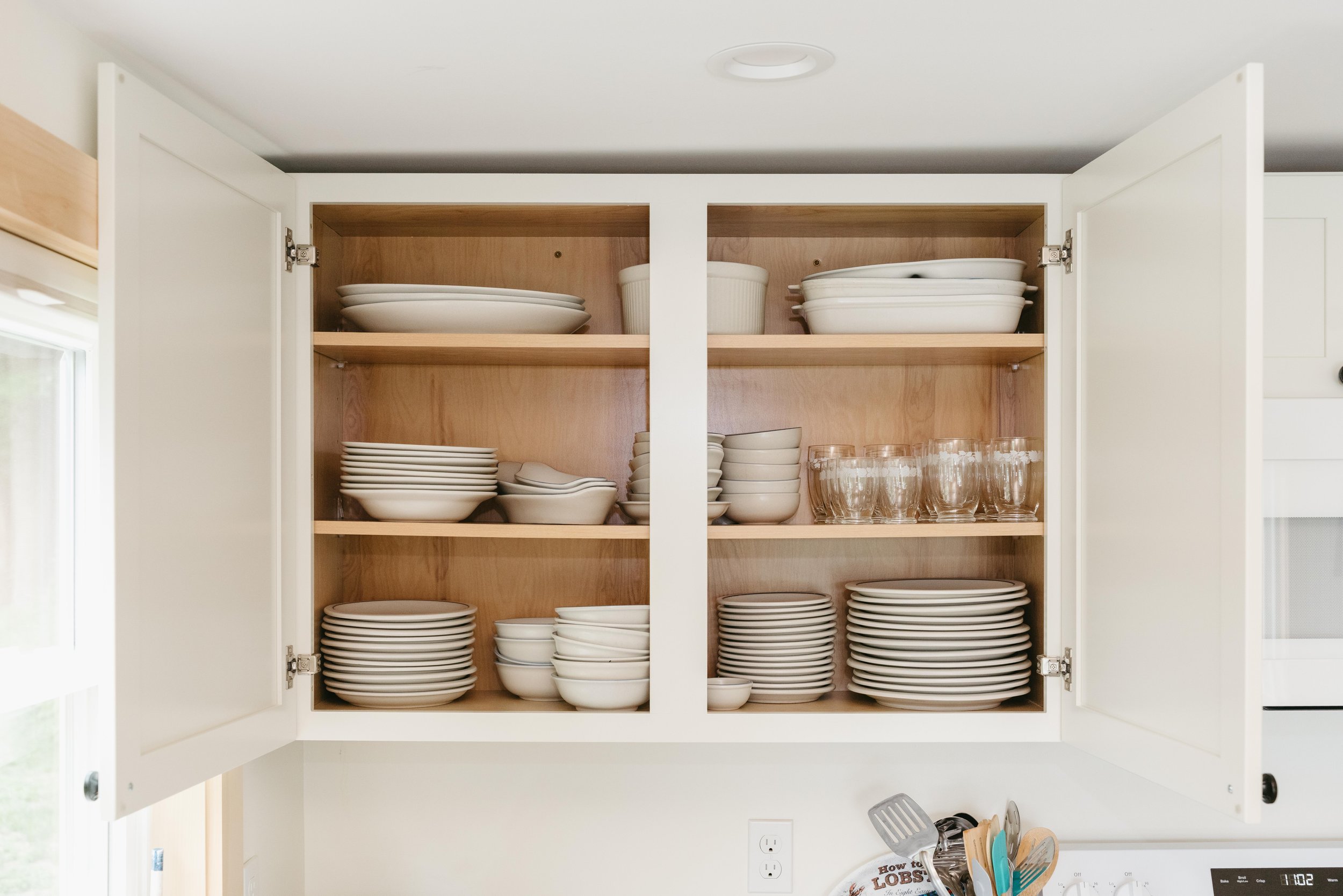 Open kitchen cabinet filled with white dishes, bowls, glasses, and plates.
