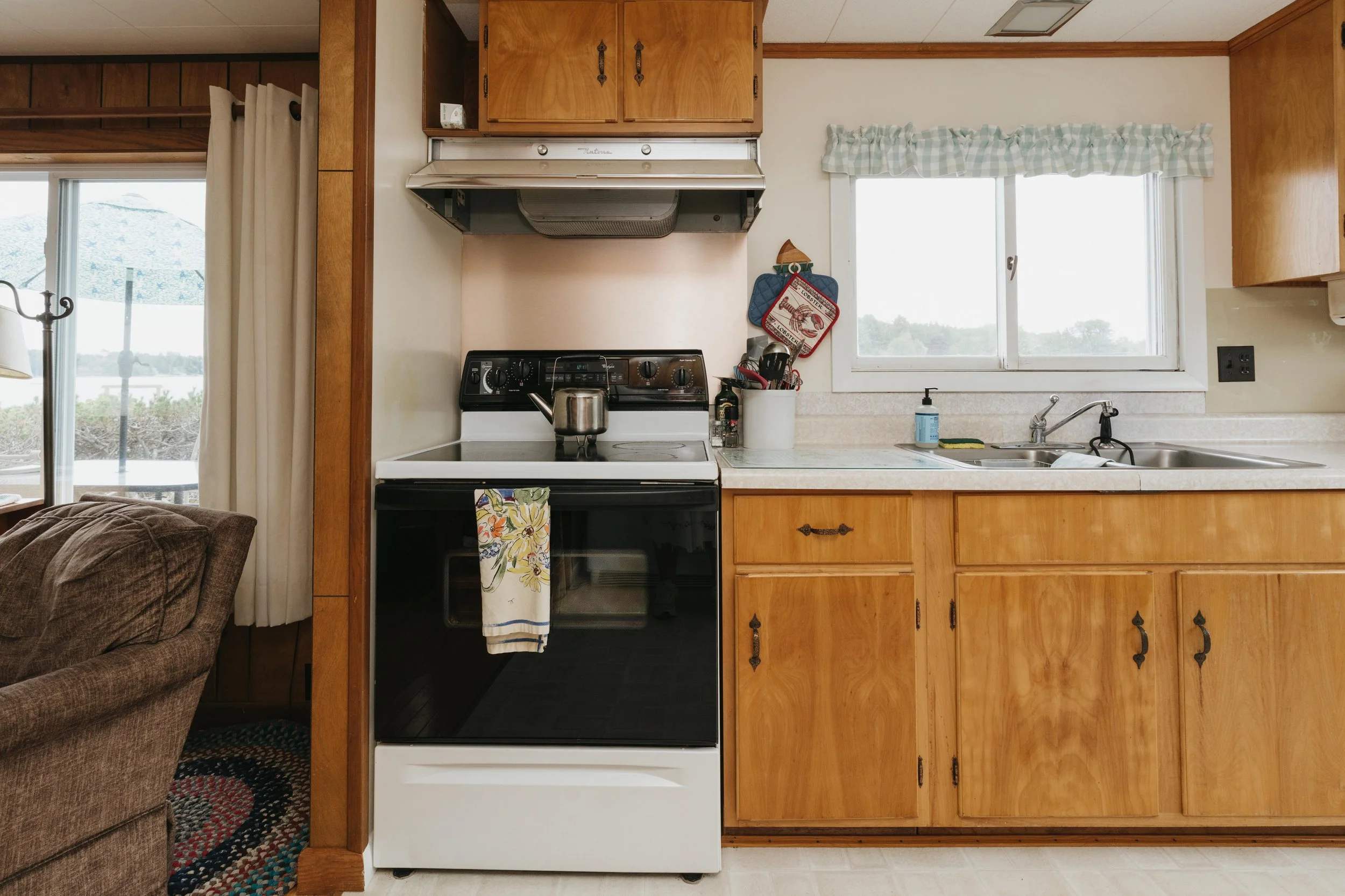 A cozy kitchen with wooden cabinets, a white stove, a window with a valance, and various kitchen items on the counter.