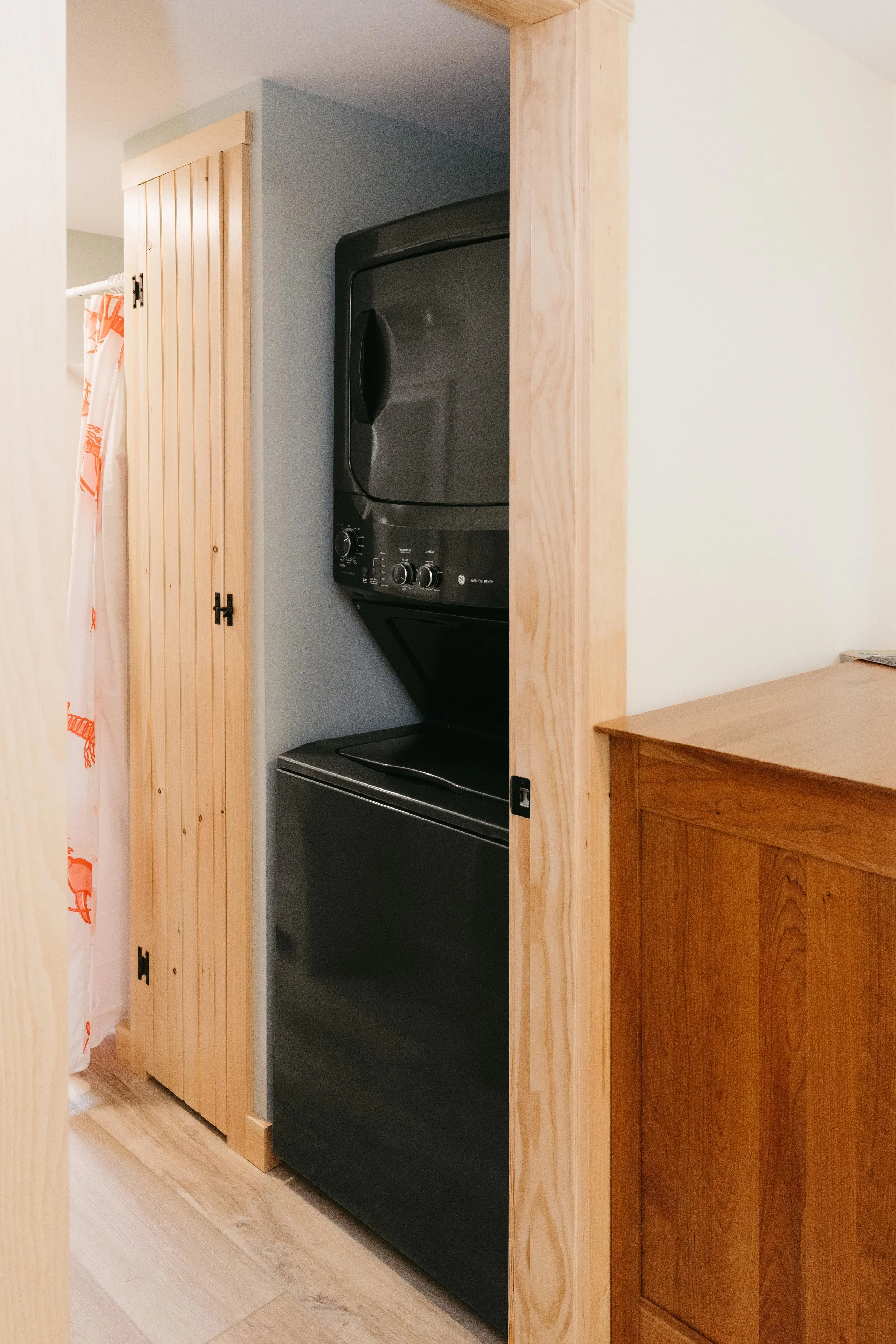 Stacked black washer and dryer inside a wooden closet in a home laundry area.