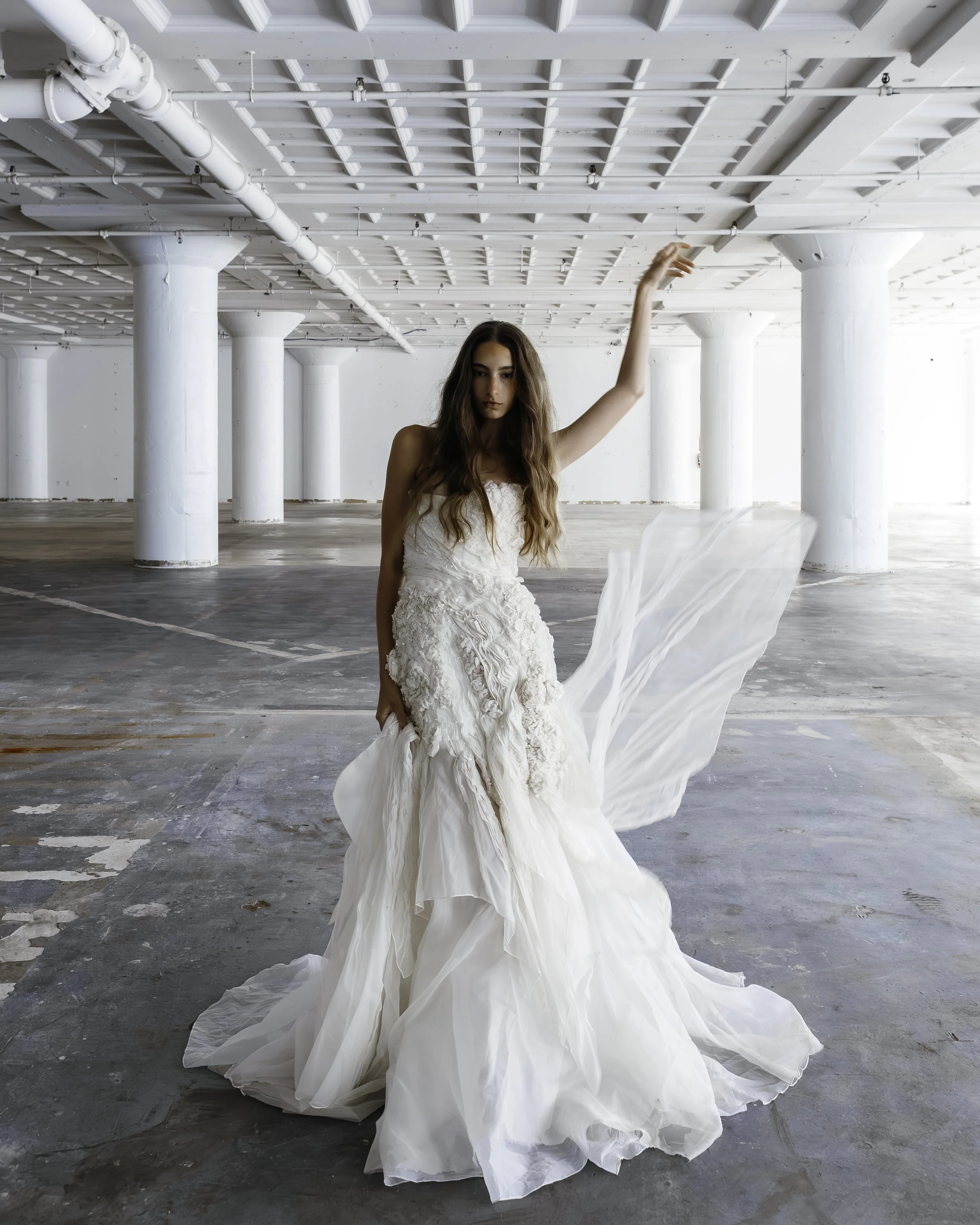 Bride in a flowing white wedding dress posing in a bright industrial loft with exposed pipes and columns