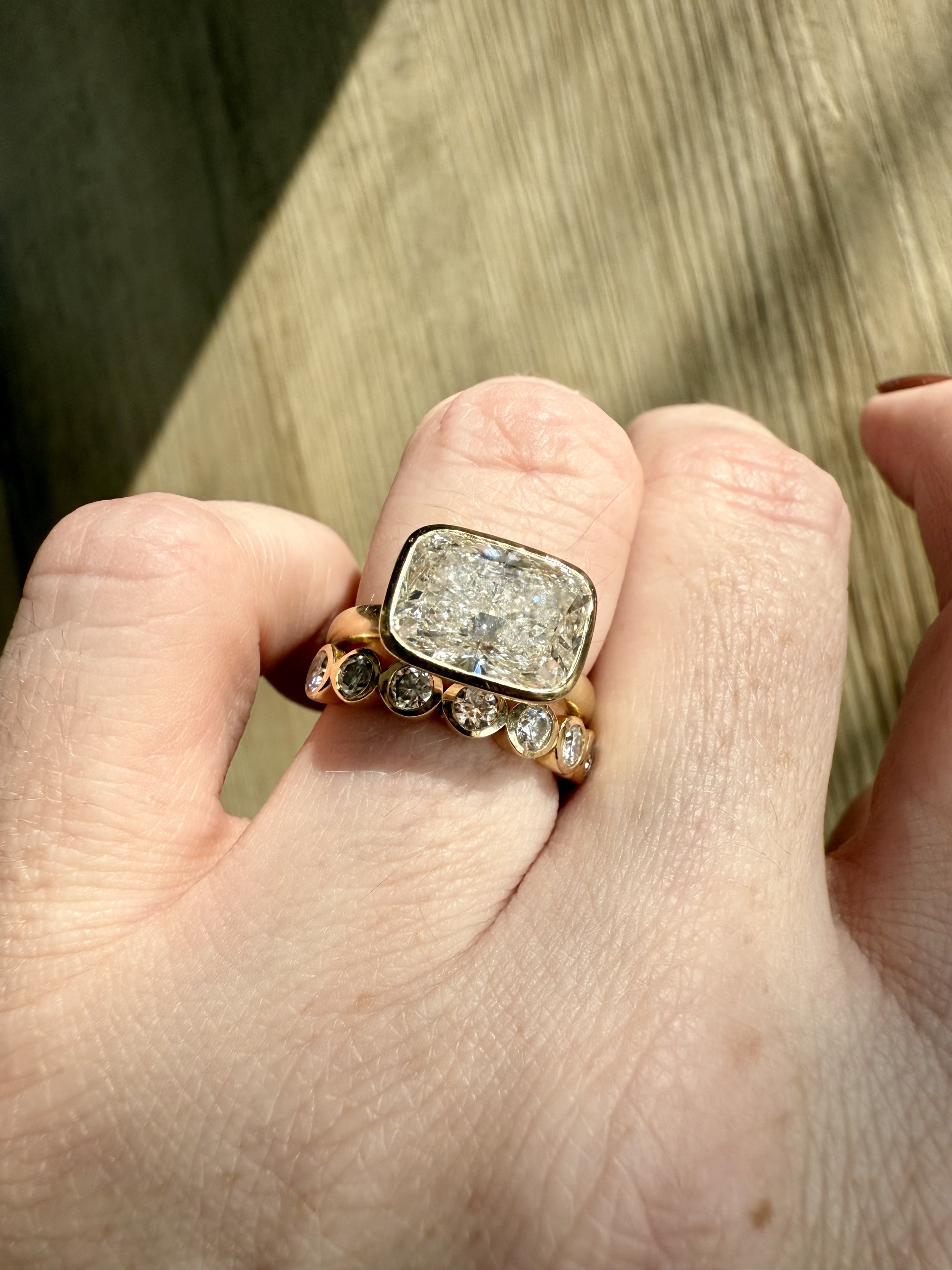 A person wearing a large gold ring with a rectangular diamond and smaller round diamonds on the band.